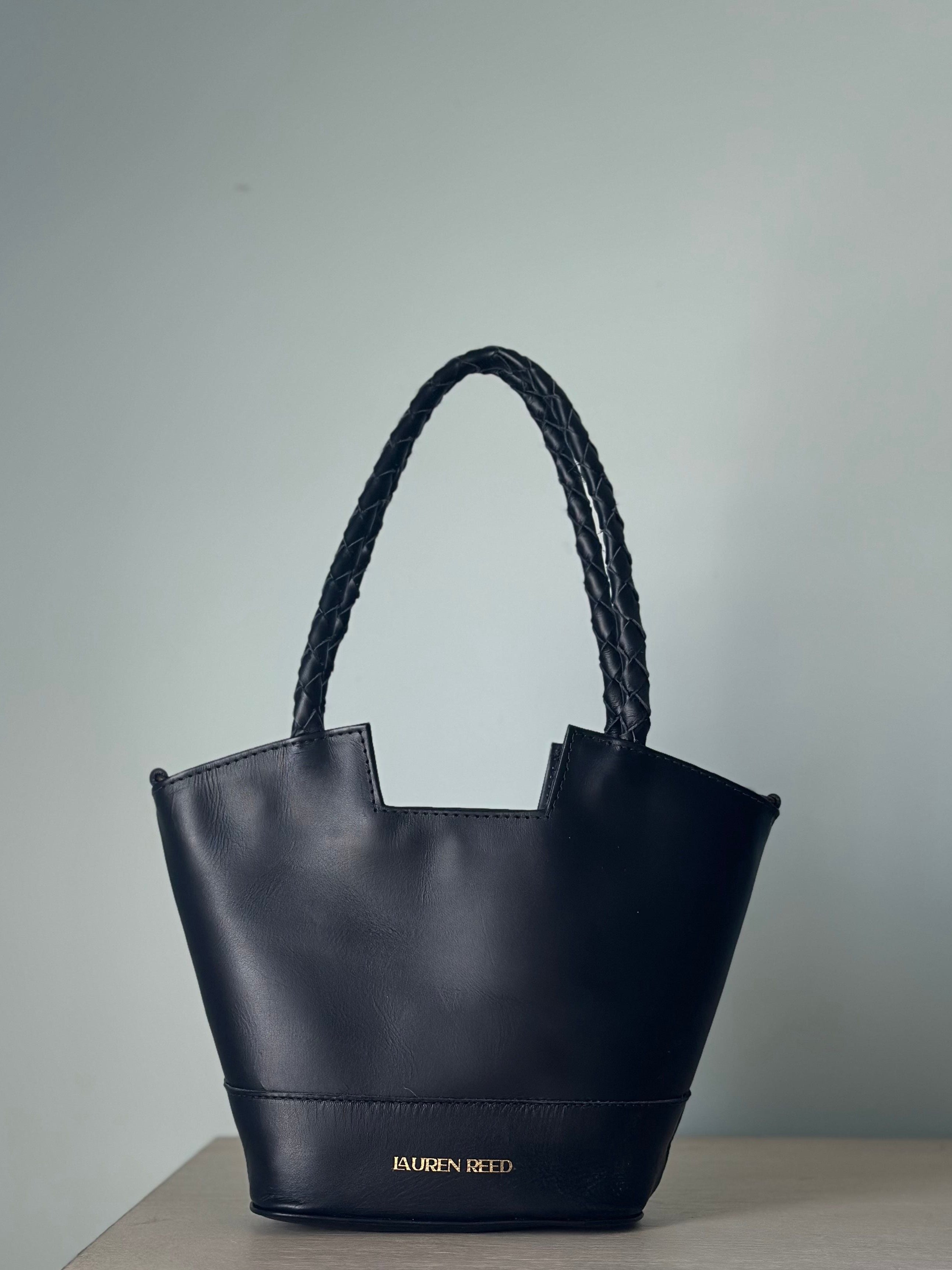 Black handbag with braided handle on a light gray background