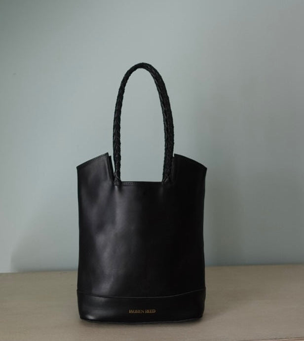 Black leather tote bag with braided handle on a neutral background