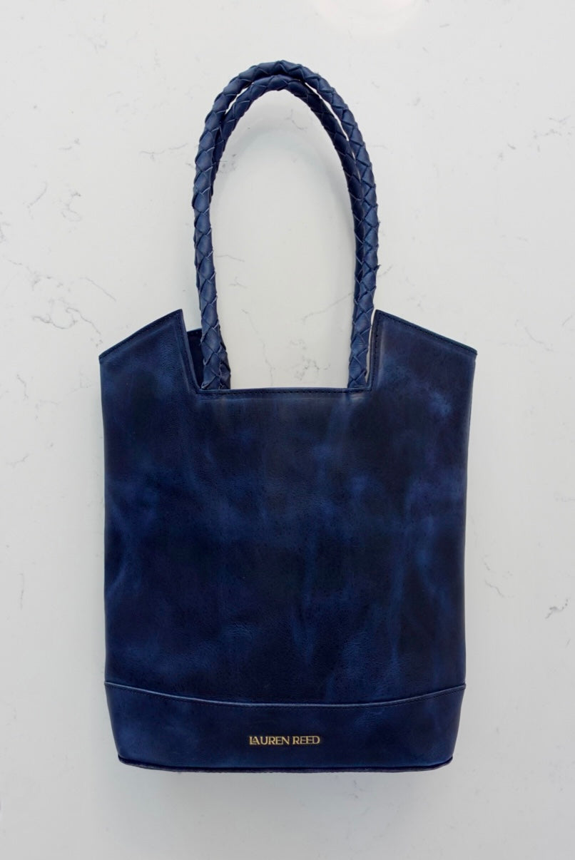 Navy blue tote bag with braided handles on a light gray background