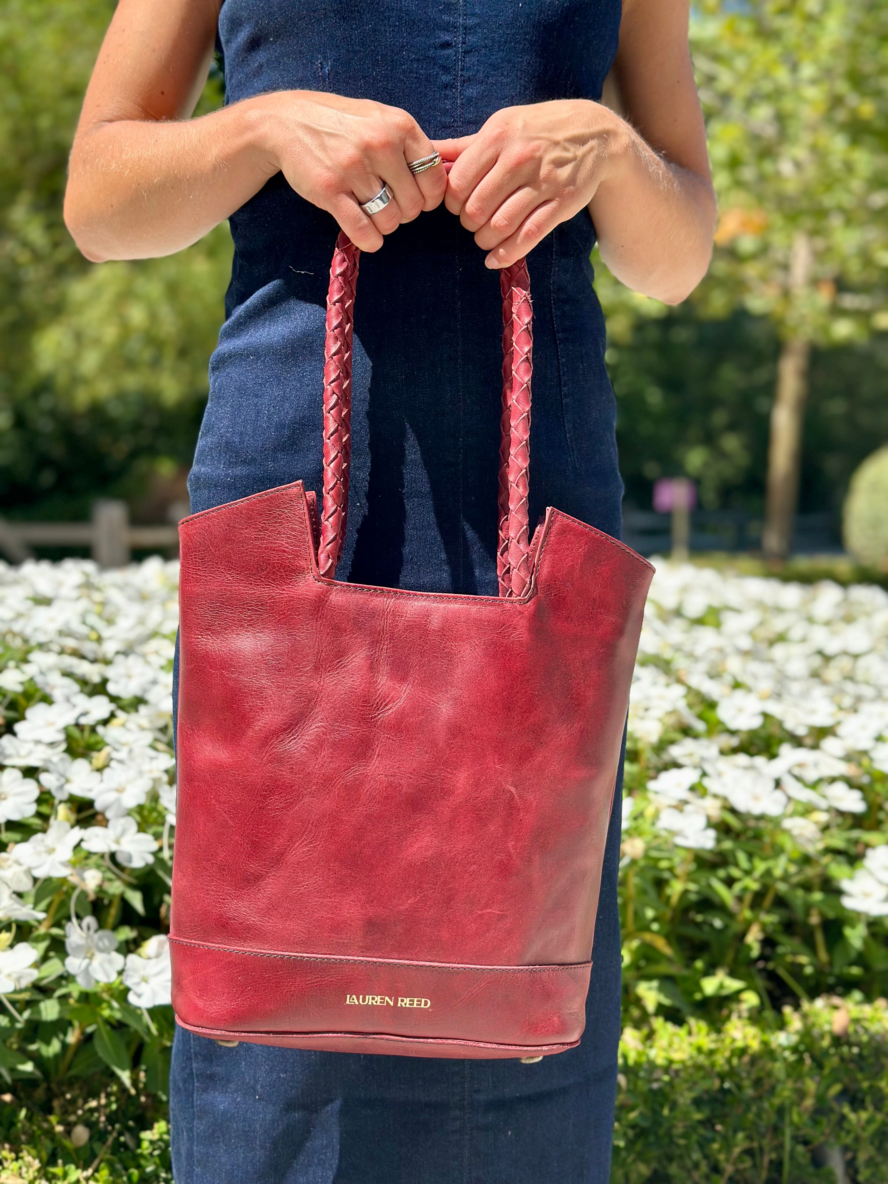 Person holding a red handbag with braided handles in an outdoor setting.