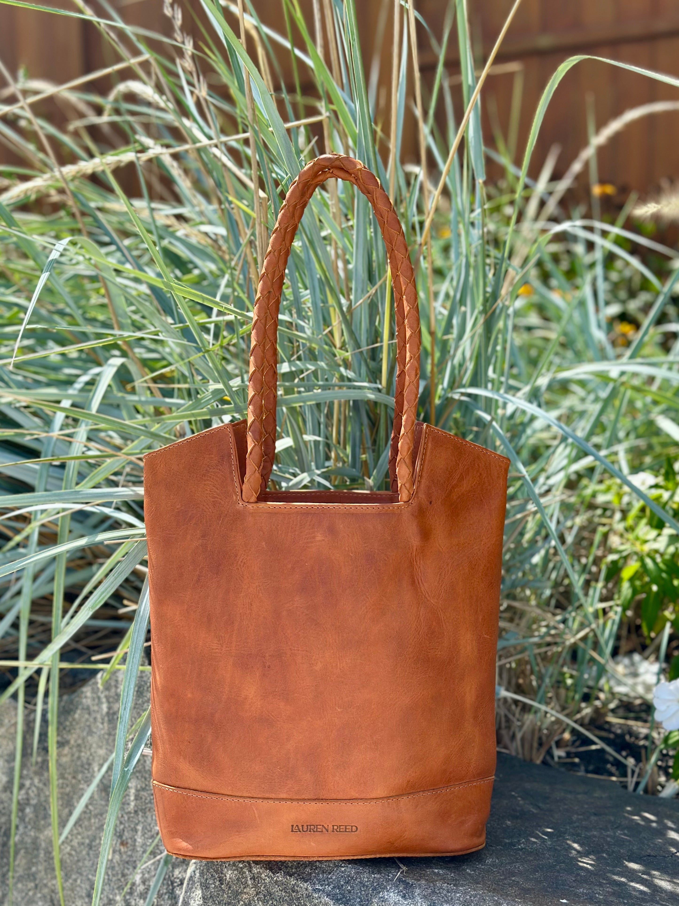 Tan leather tote bag on a stone surface with grass in the background