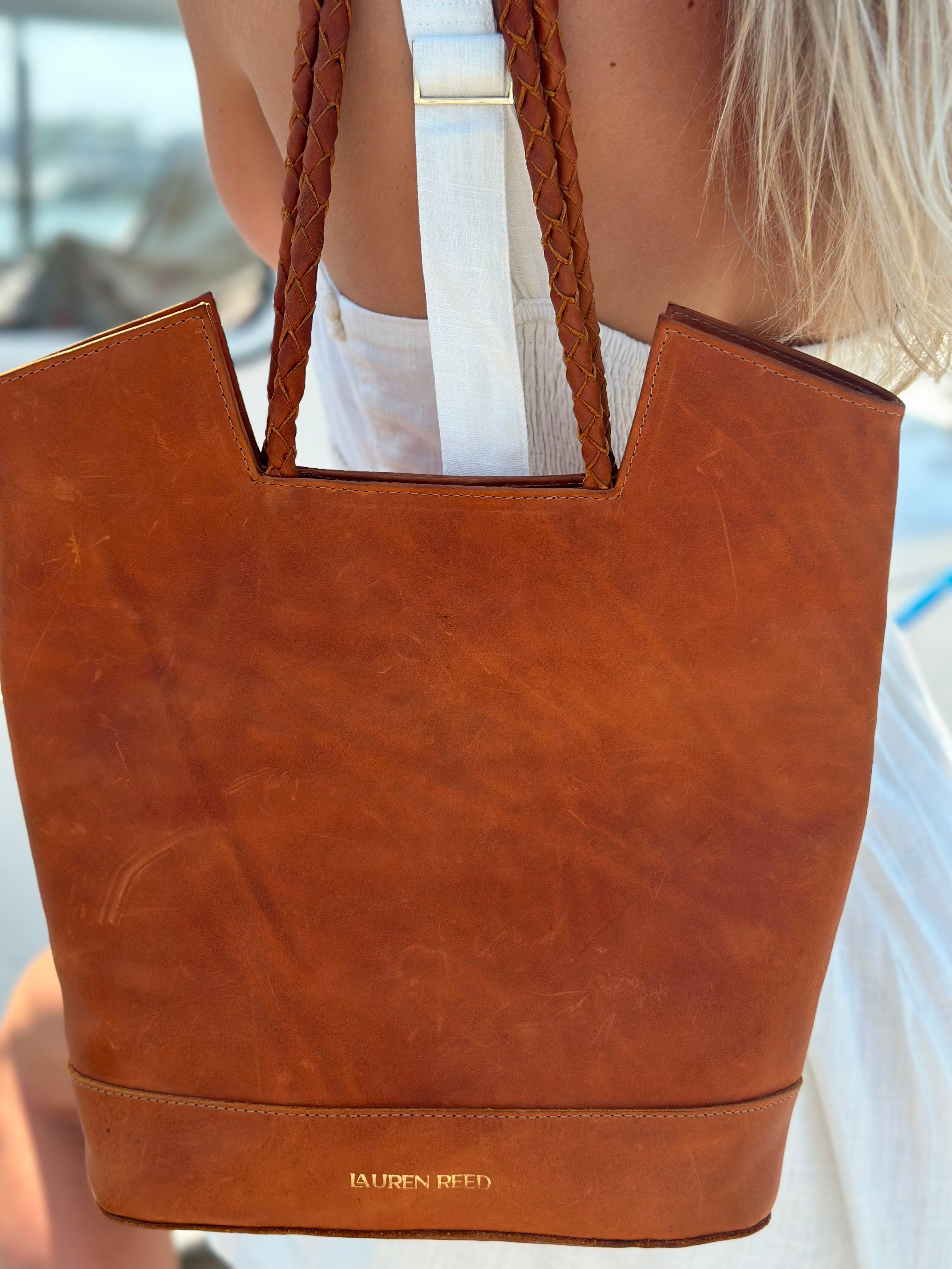 Brown leather tote bag with 'Lauren Reed' branding held by a person.