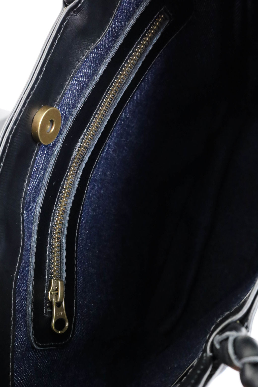 Close-up of a black leather bag with zipper and magnetic button details.