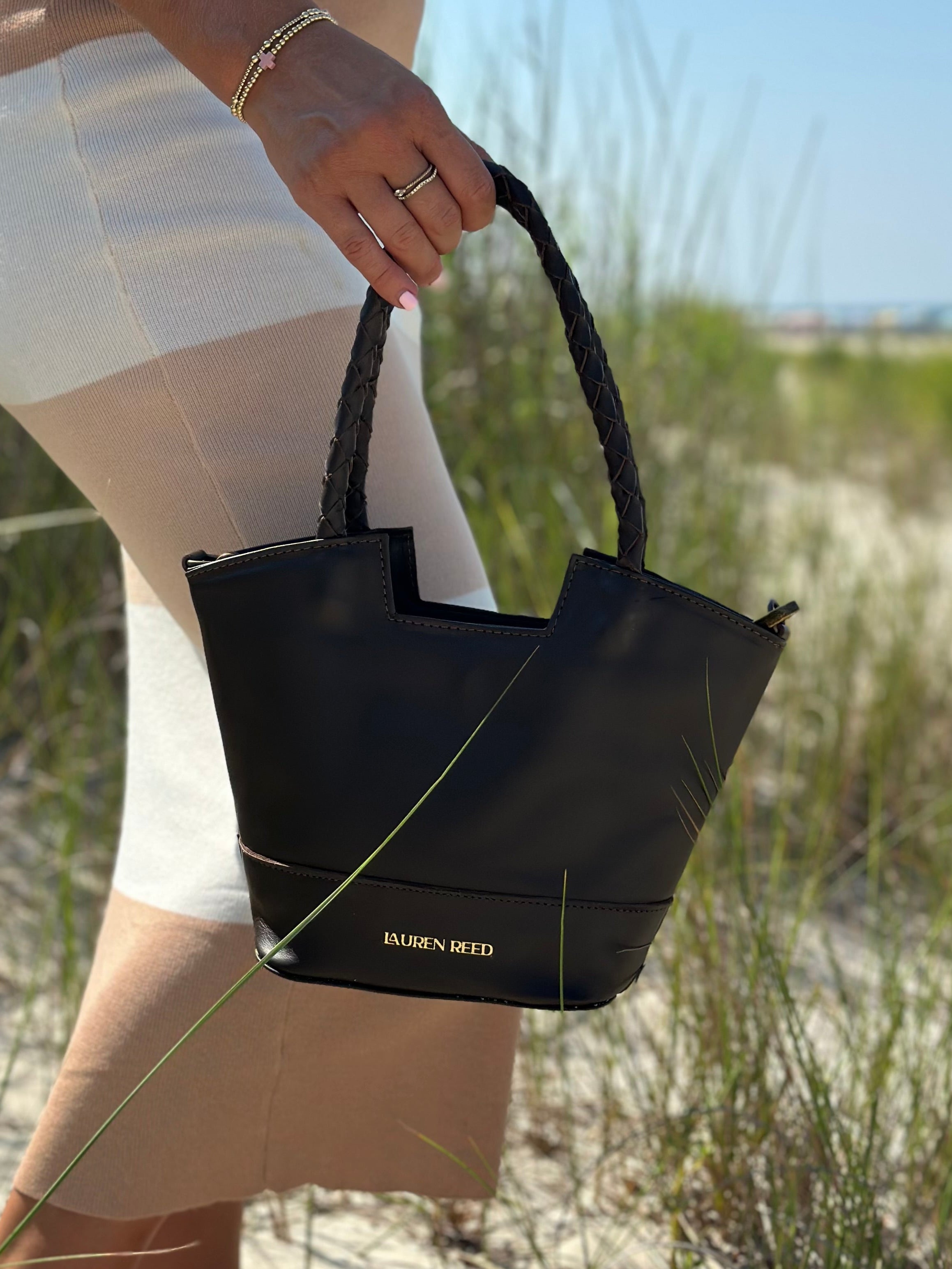 Person holding a black handbag with a blurred natural background