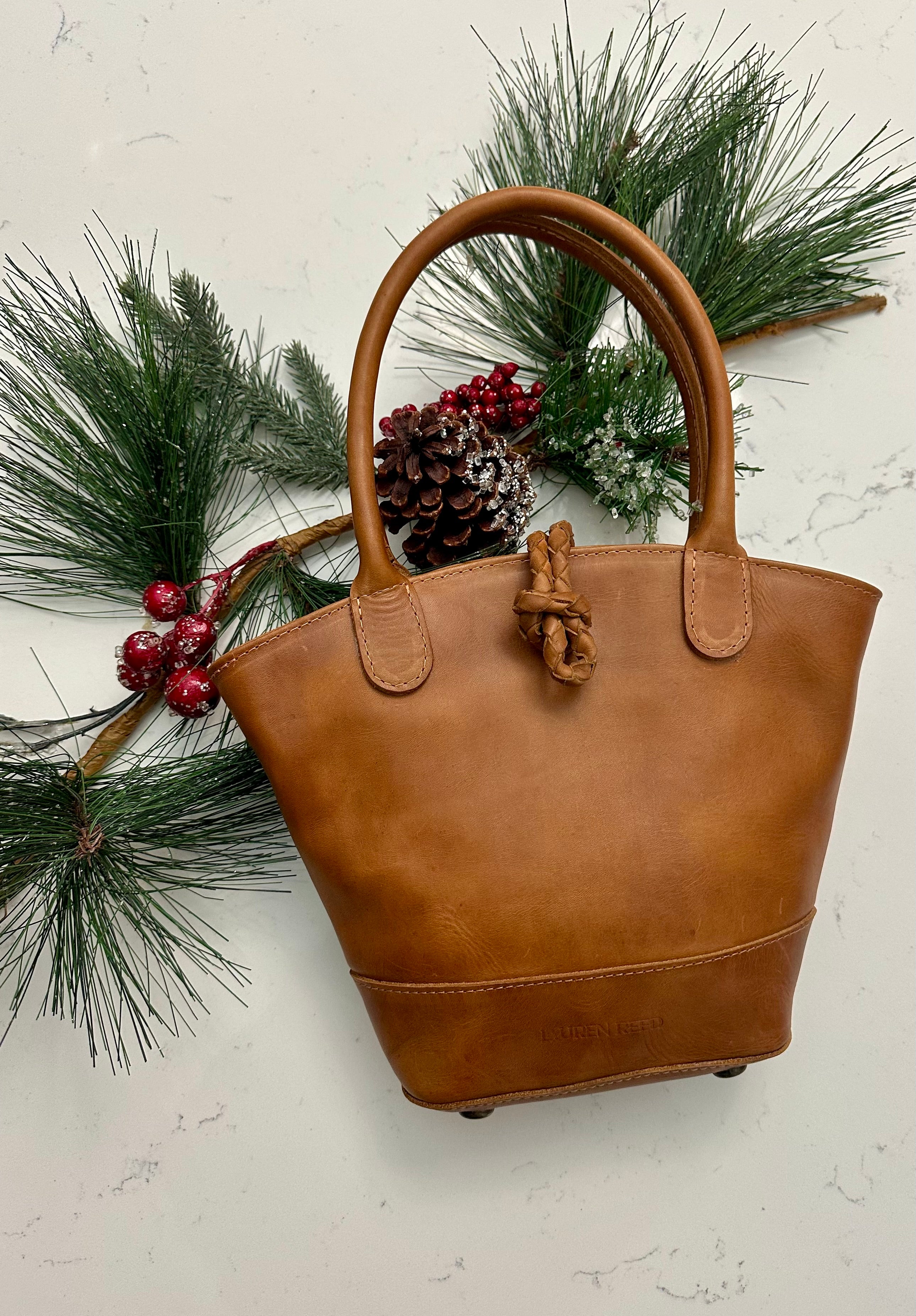 Tan leather handbag with decorative elements on a light background