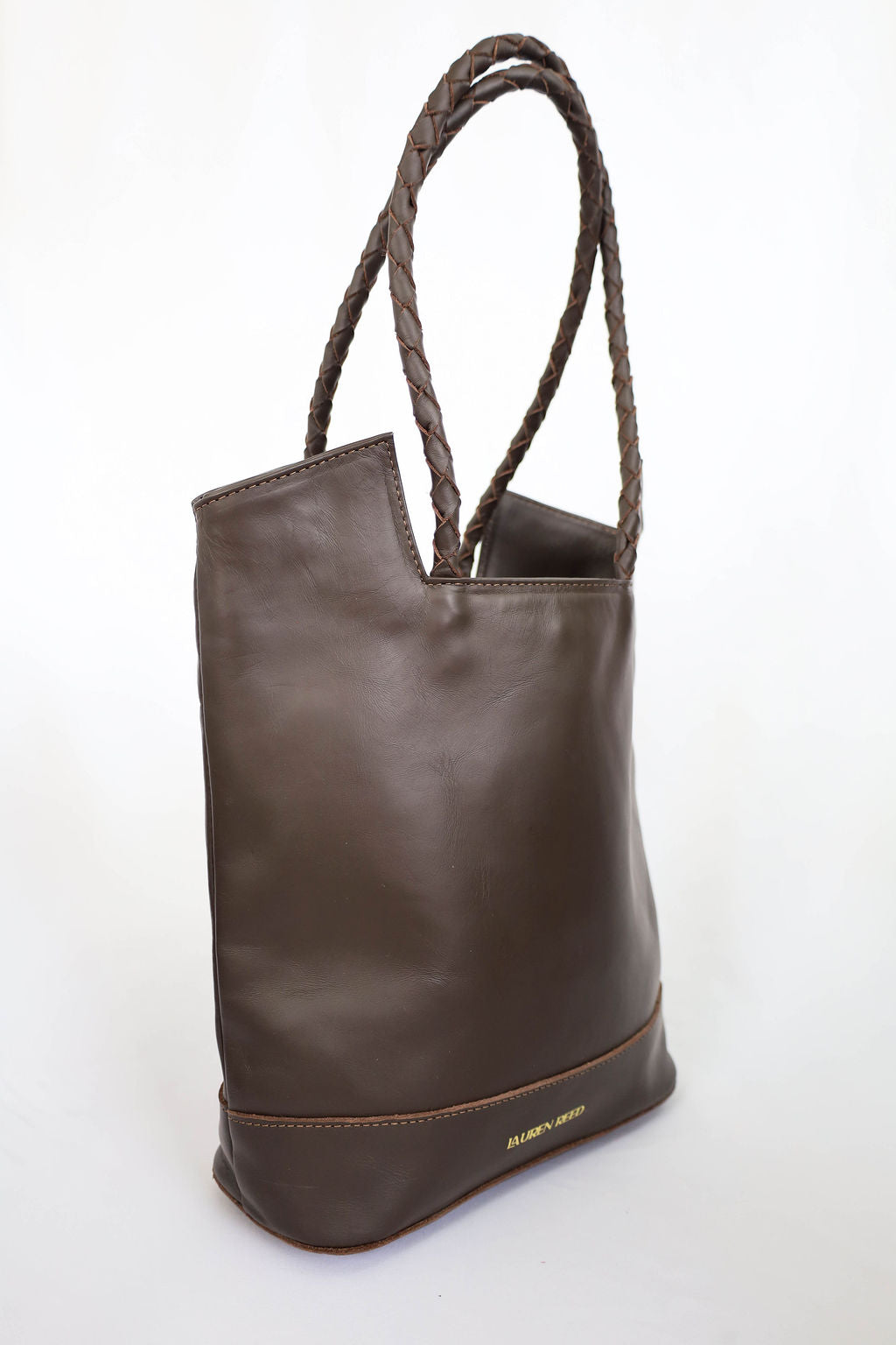 Brown leather tote bag with braided handle on a white background