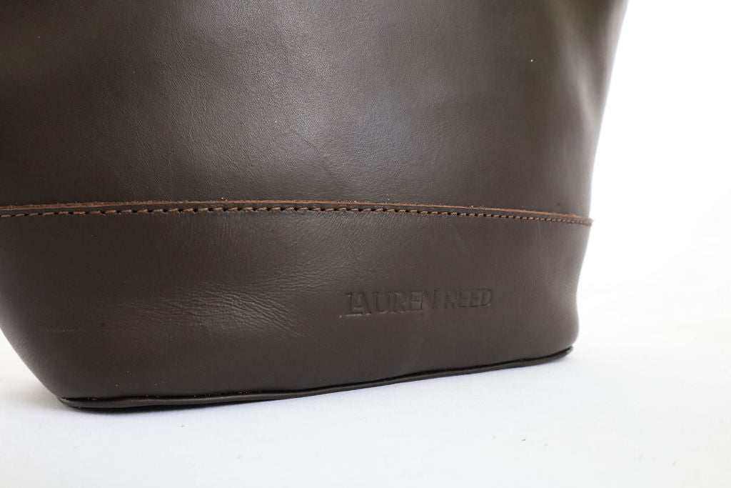 Close-up of a brown leather bag with 'Lauren Reed' branding on a white background
