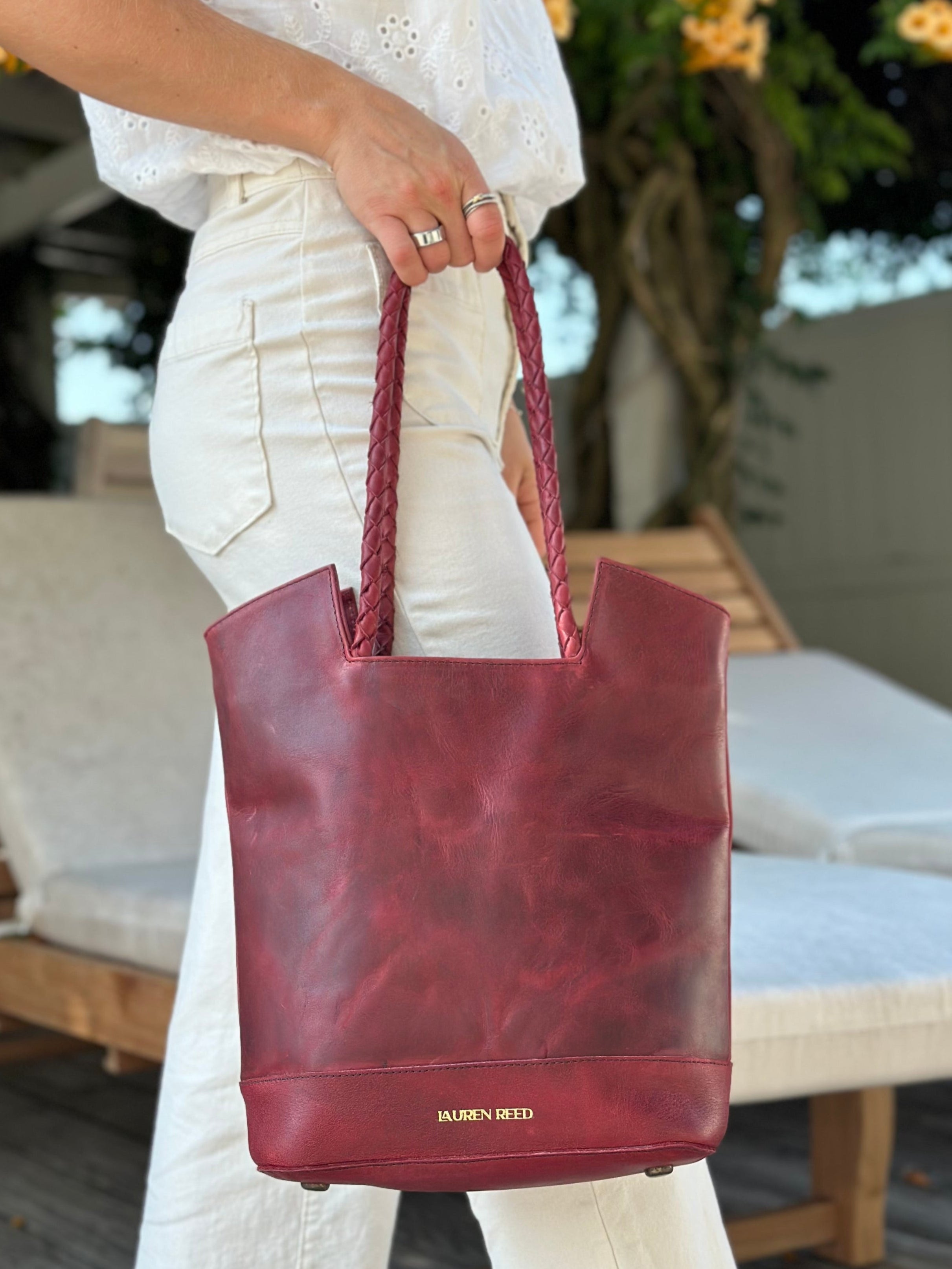 Person holding a maroon handbag with a blurred outdoor background