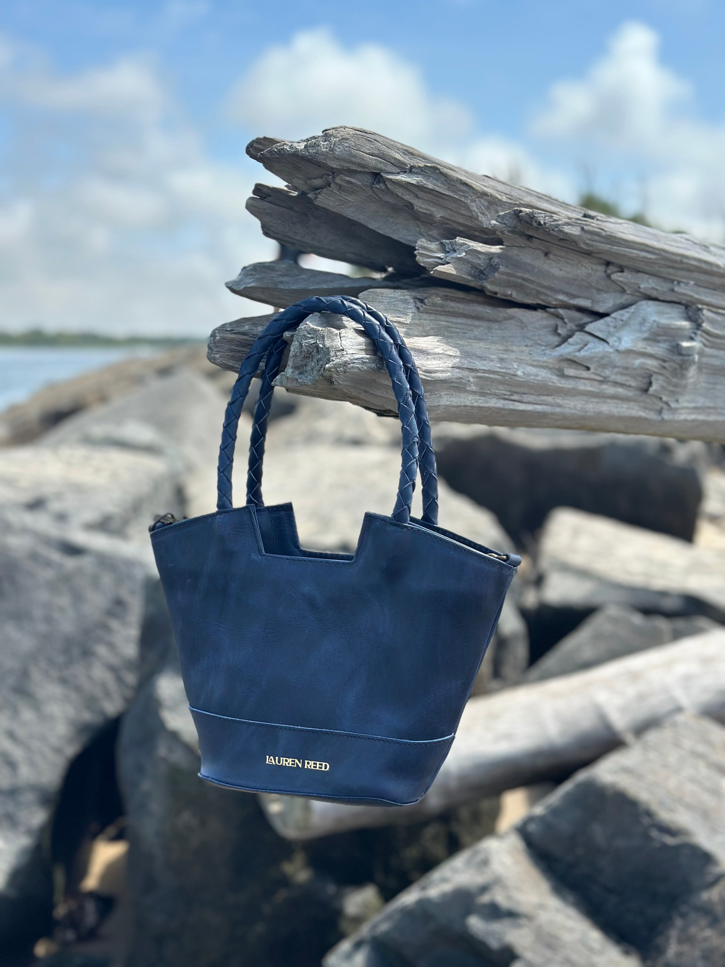 Blue leather handbag on a piece of beach driftwood with a blurred natural background