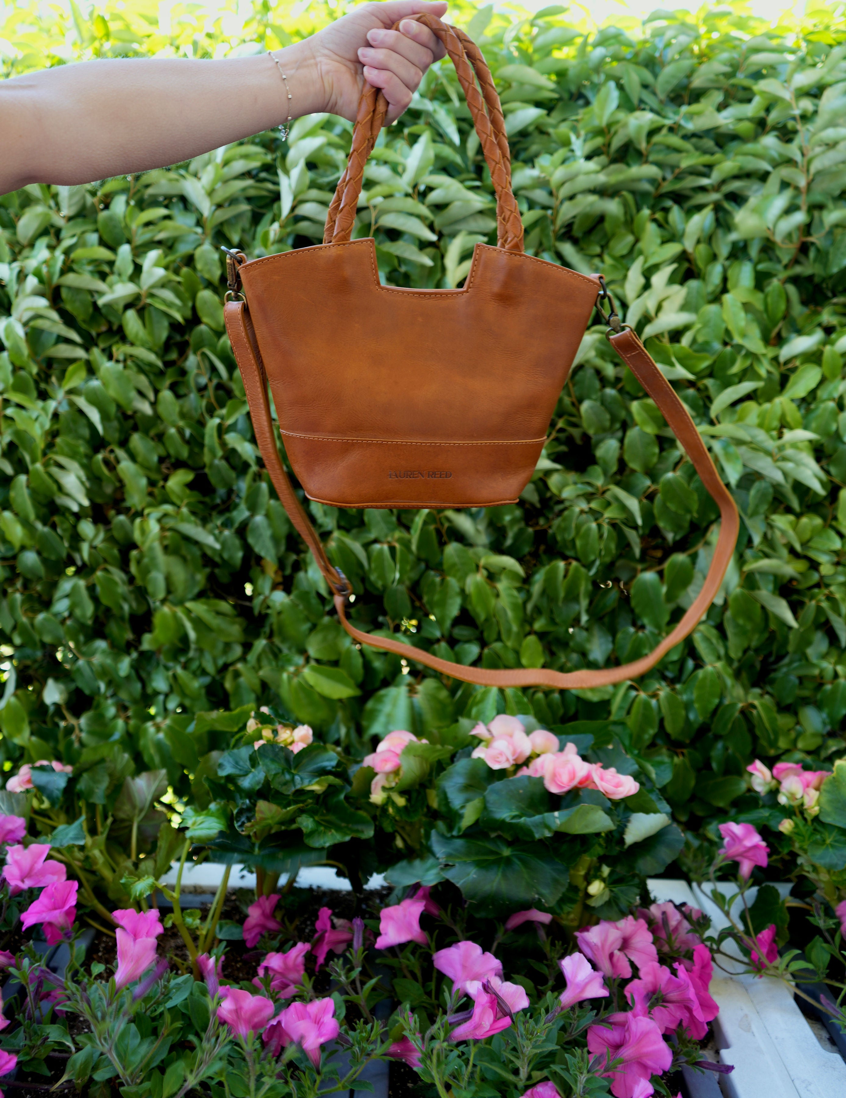 Lauren Reed Co Leather Crossbody Purse with Braided Handles held above flowers