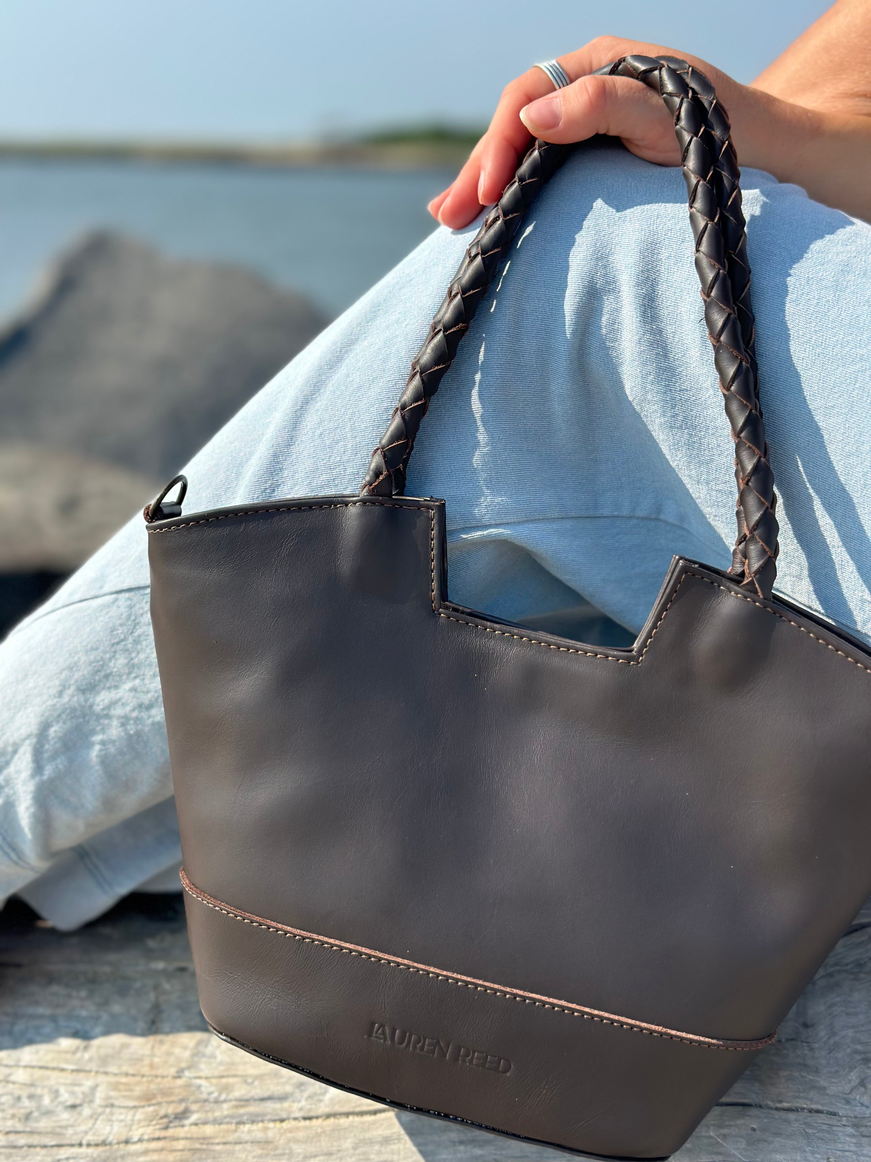 Brown leather handbag with braided handle held by a person.