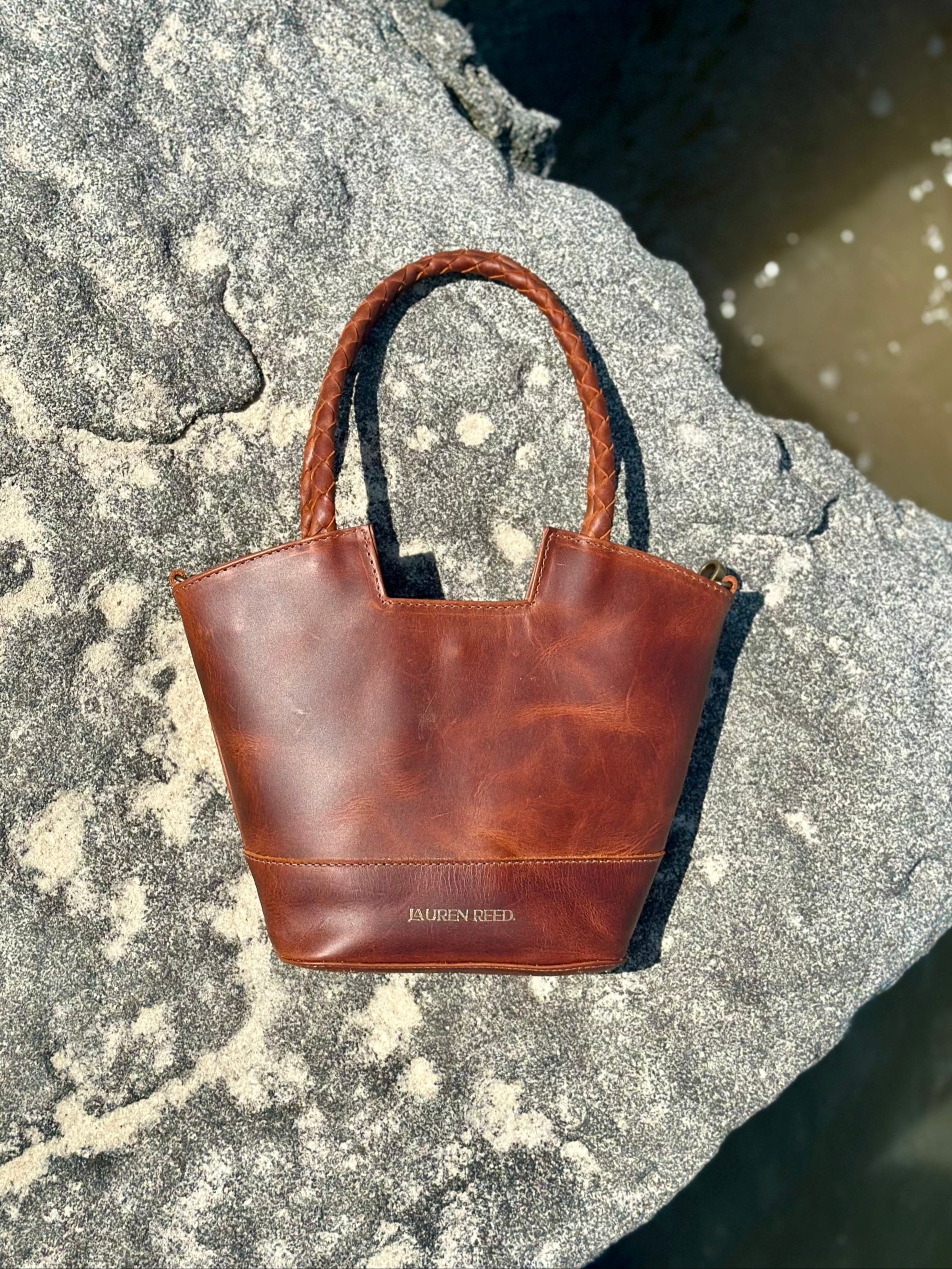 Brown leather handbag on a rocky surface near water