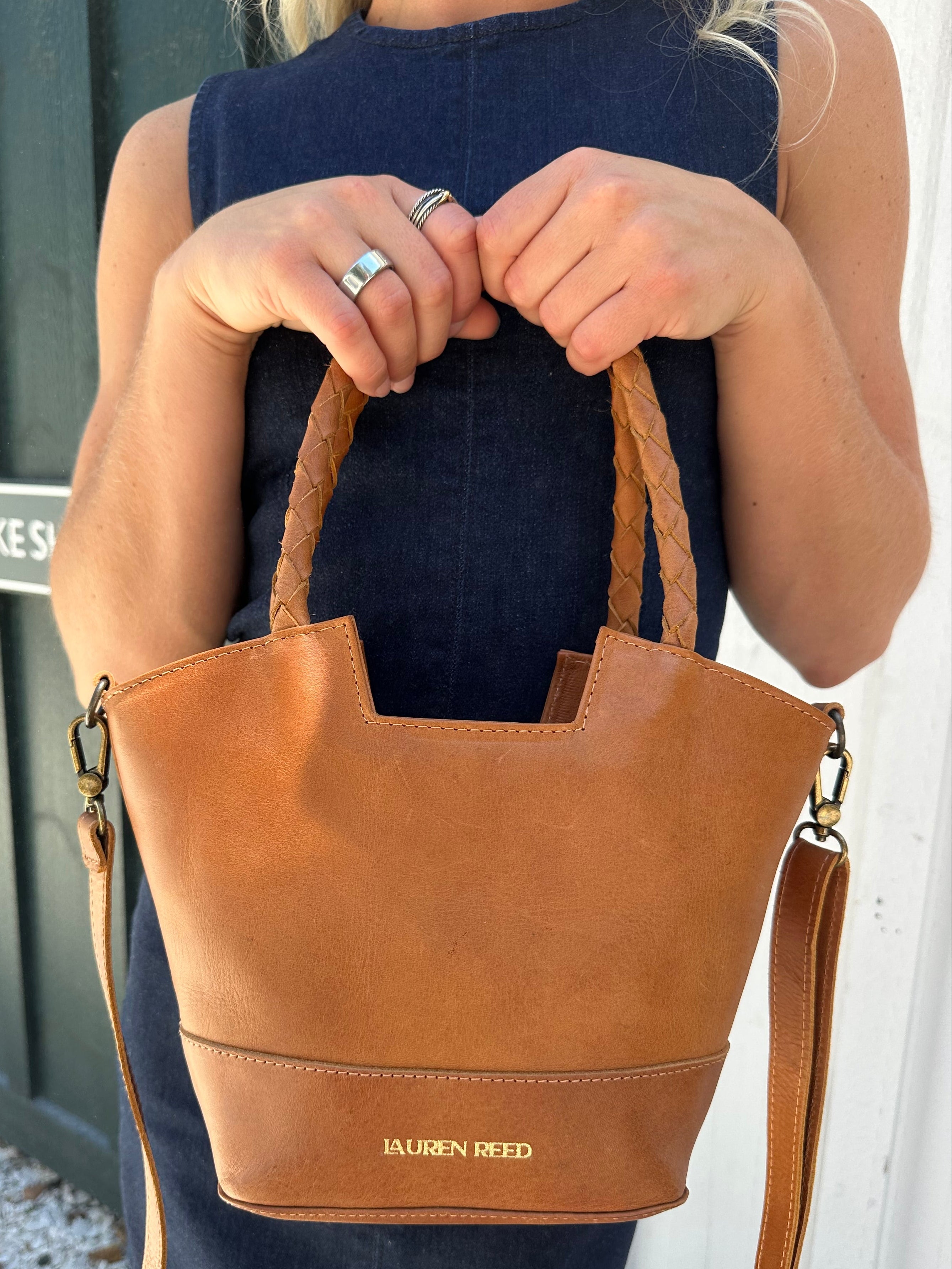 Person holding a tan leather handbag with visible branding "Lauren Reed"