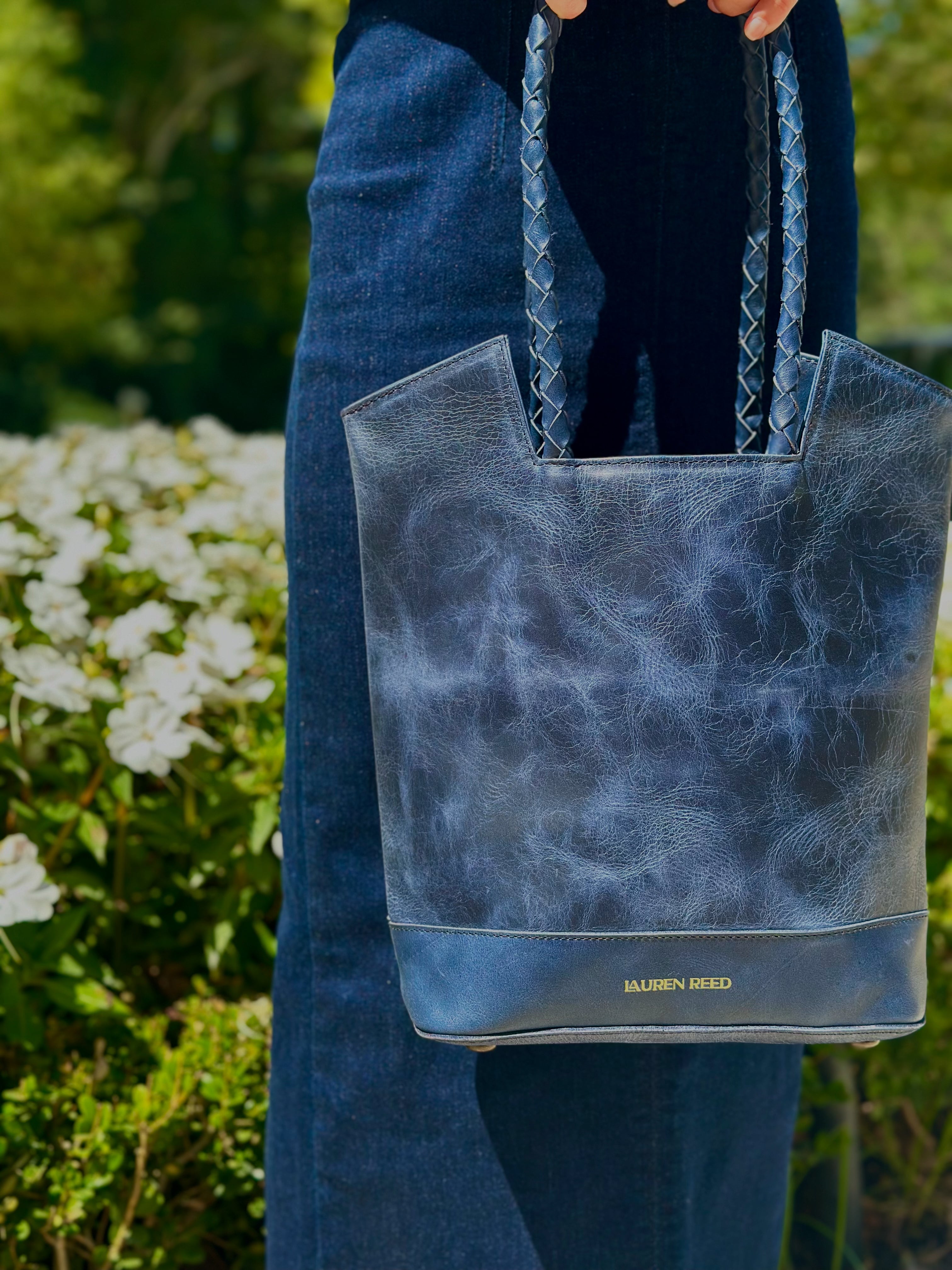 Blue leather tote bag held by a person with a blurred natural background