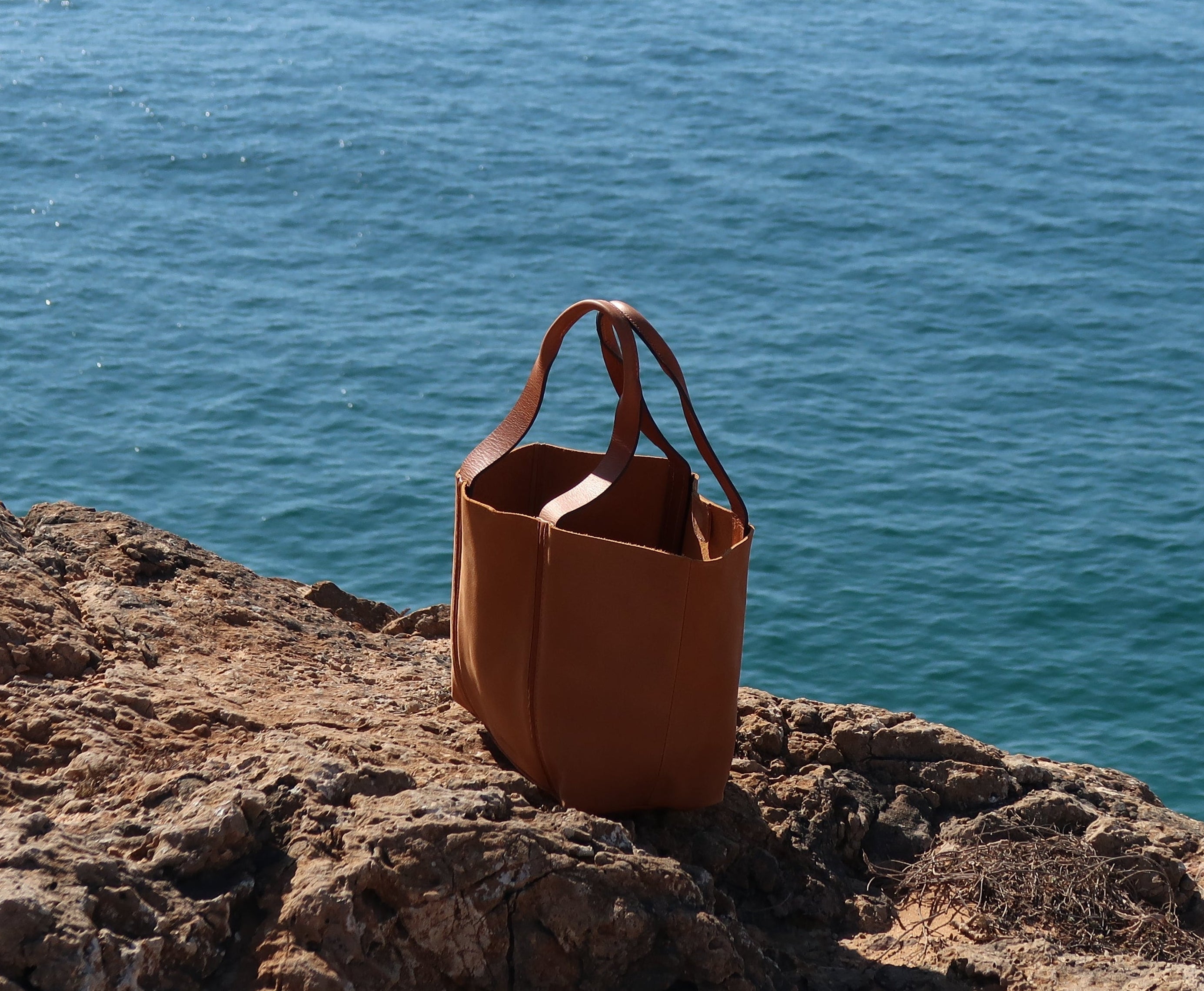 Tan nubuck leather bag on a rocky cliff overlooking the ocean