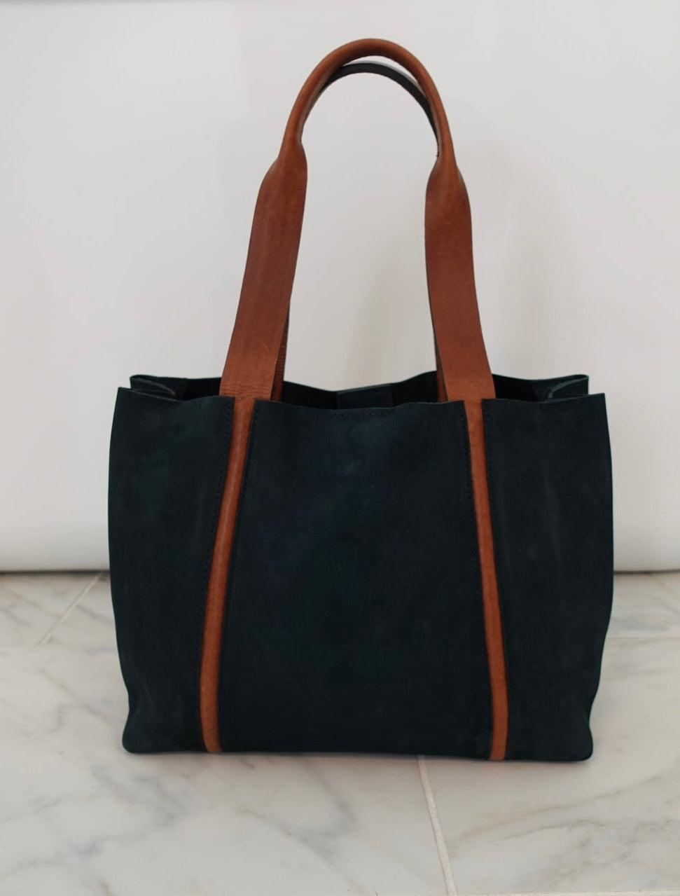 Blue tote bag with brown straps on a white marble surface