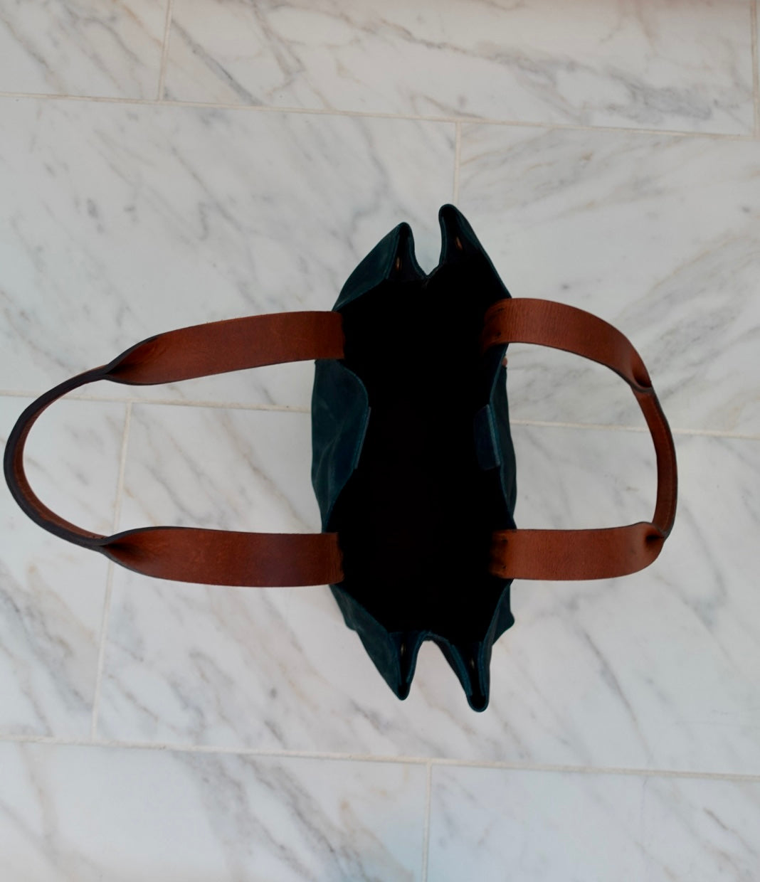 Blue leather bag with brown straps on a marble surface