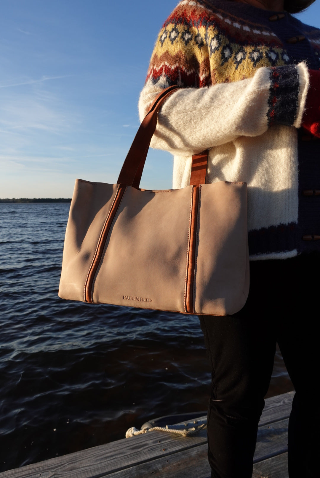 Beige bag held by a person wearing a patterned sweater against a blue sky.