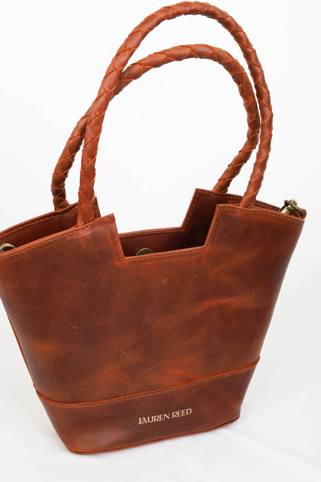 Brown leather tote bag with braided handles on a white background