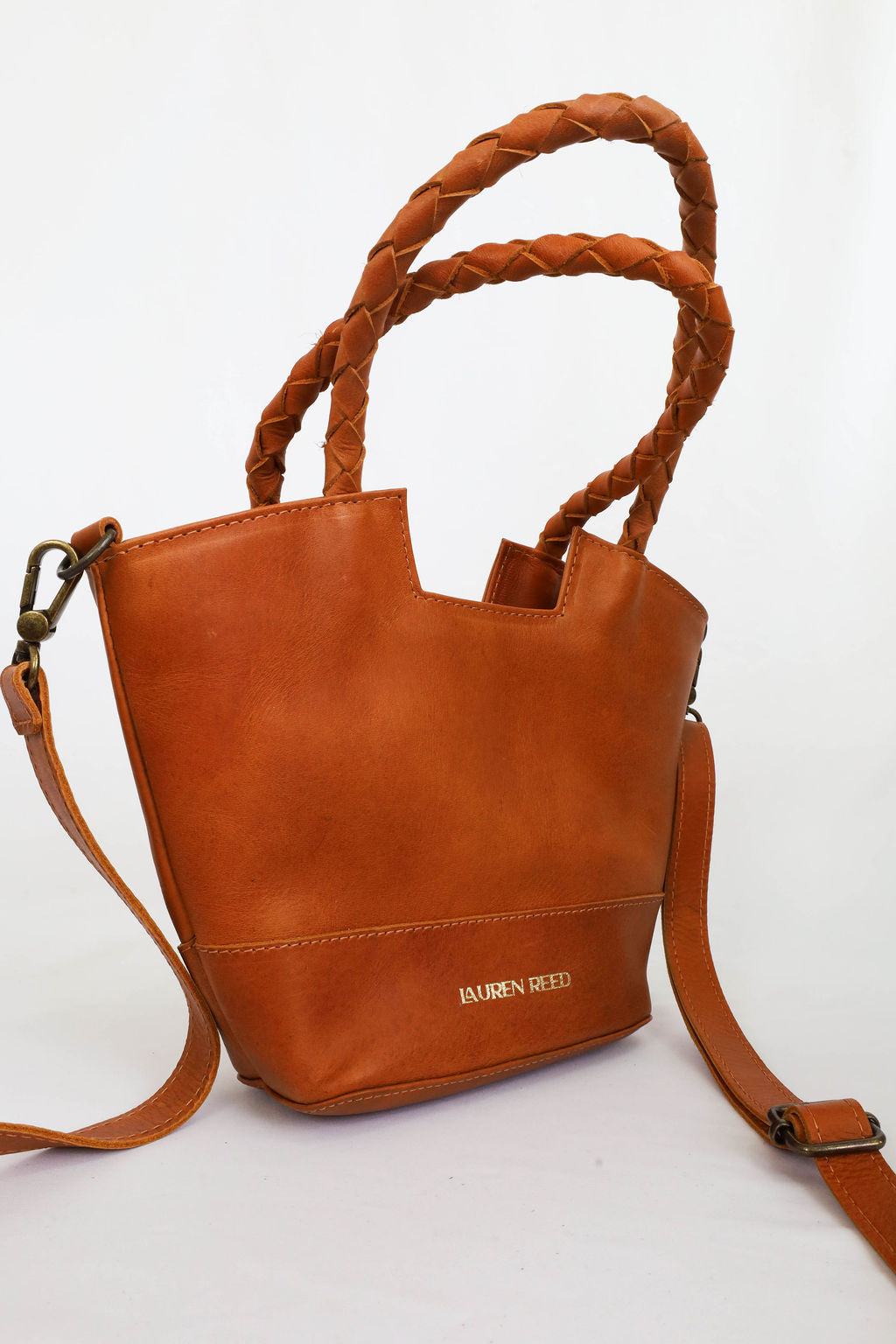 Tan leather handbag with braided handles on a white background