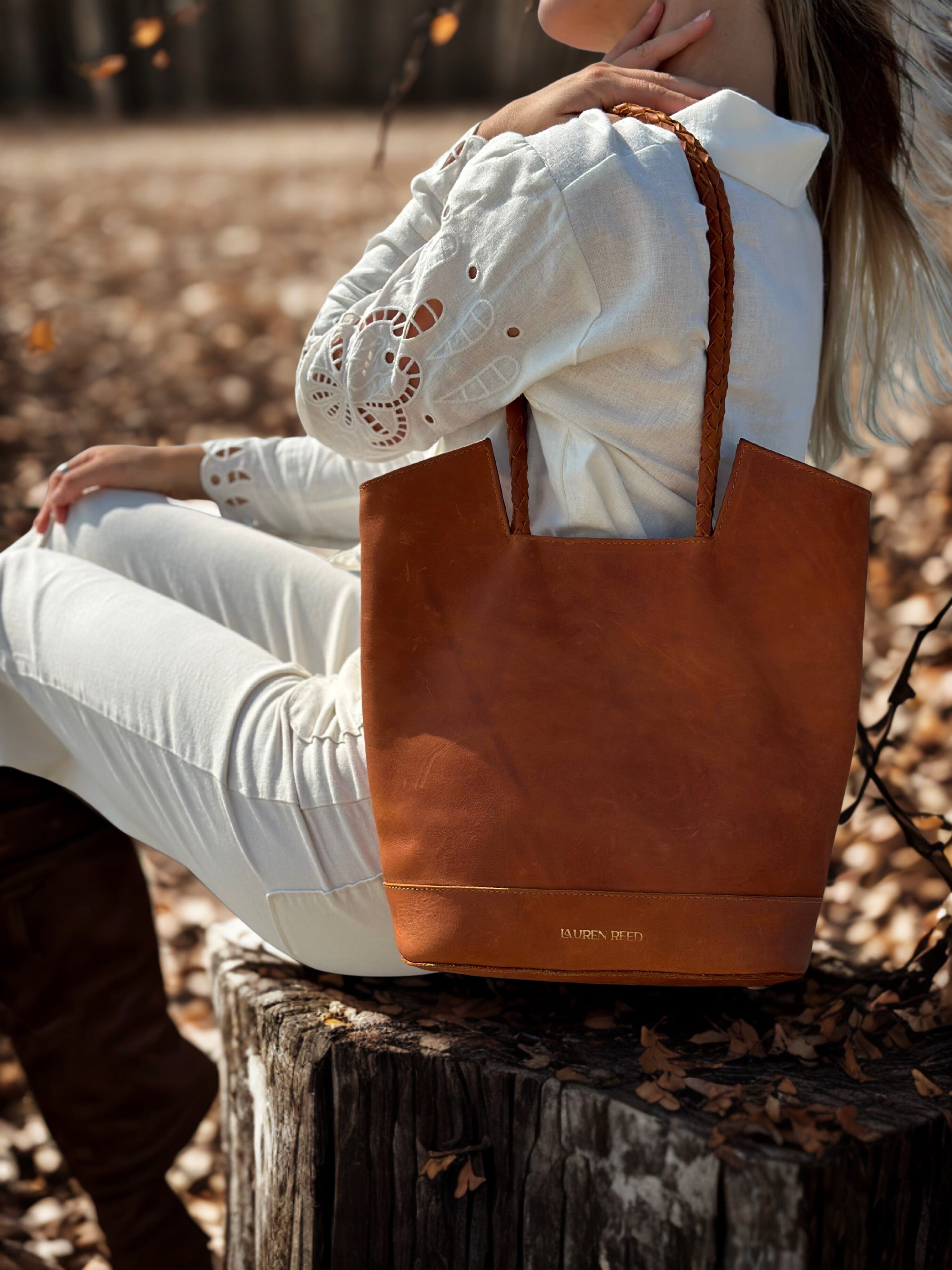 Person sitting on a log with a brown leather tote bag