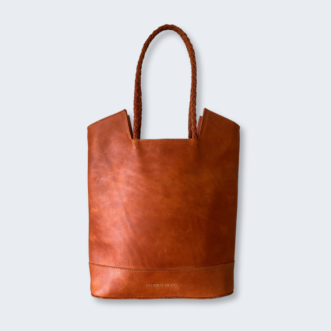 Tan leather tote bag with braided handle on a white background