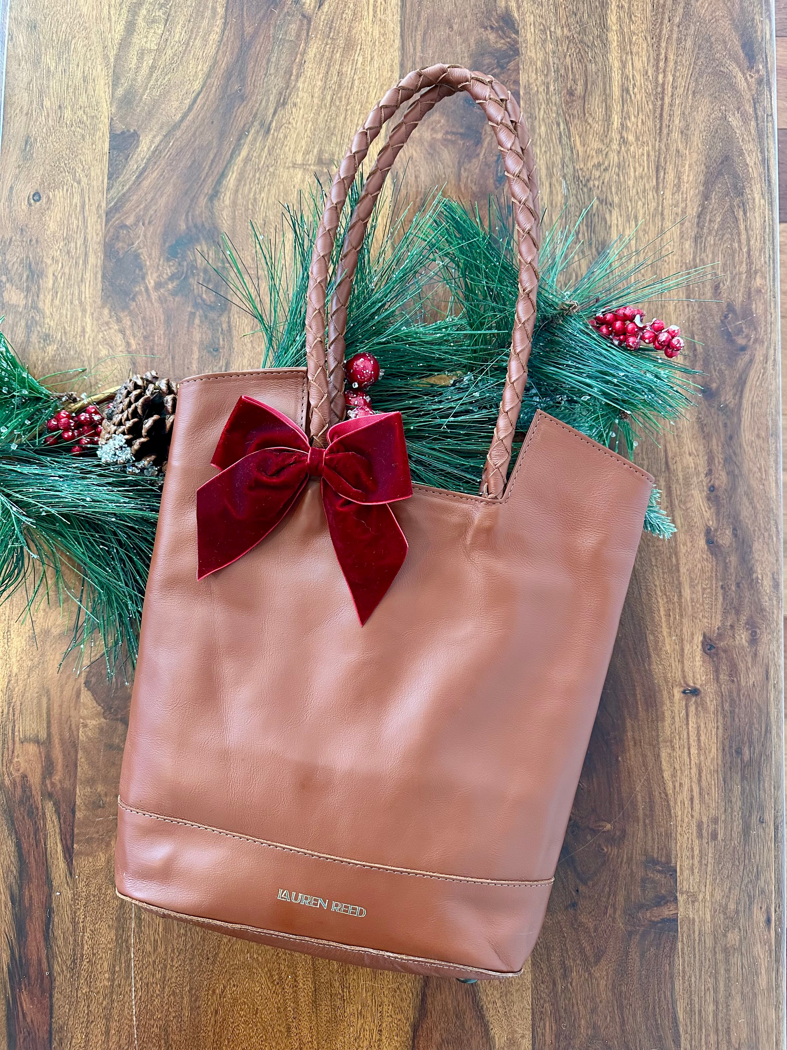 Brown leather tote bag with a red bow and greenery on a wooden background