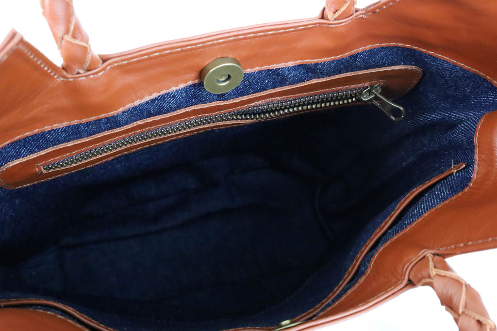 Close-up of a brown leather handbag with denim interior lining and zipper.