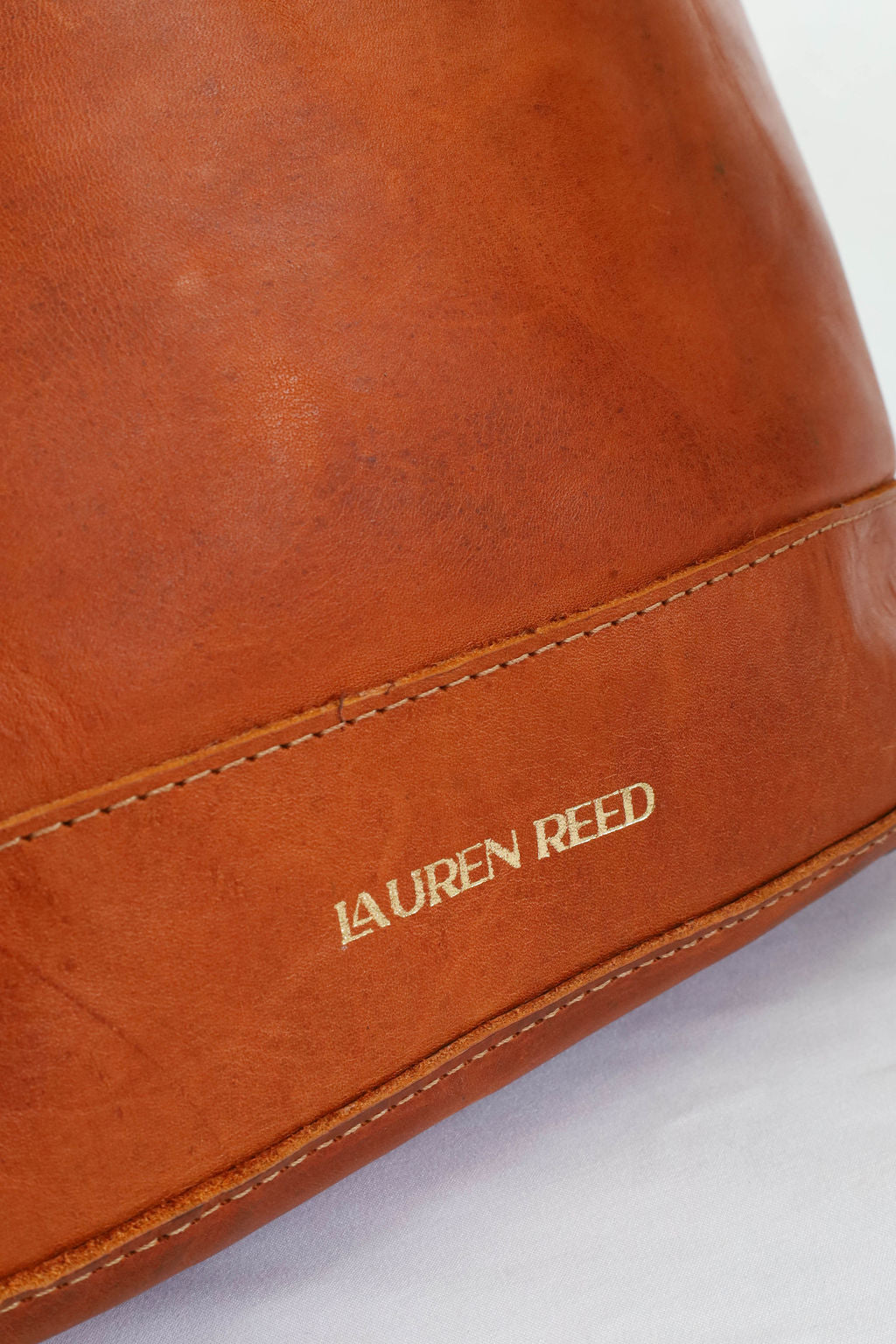 Close-up of a tan leather bag with 'Lauren Reed' branding on a white background