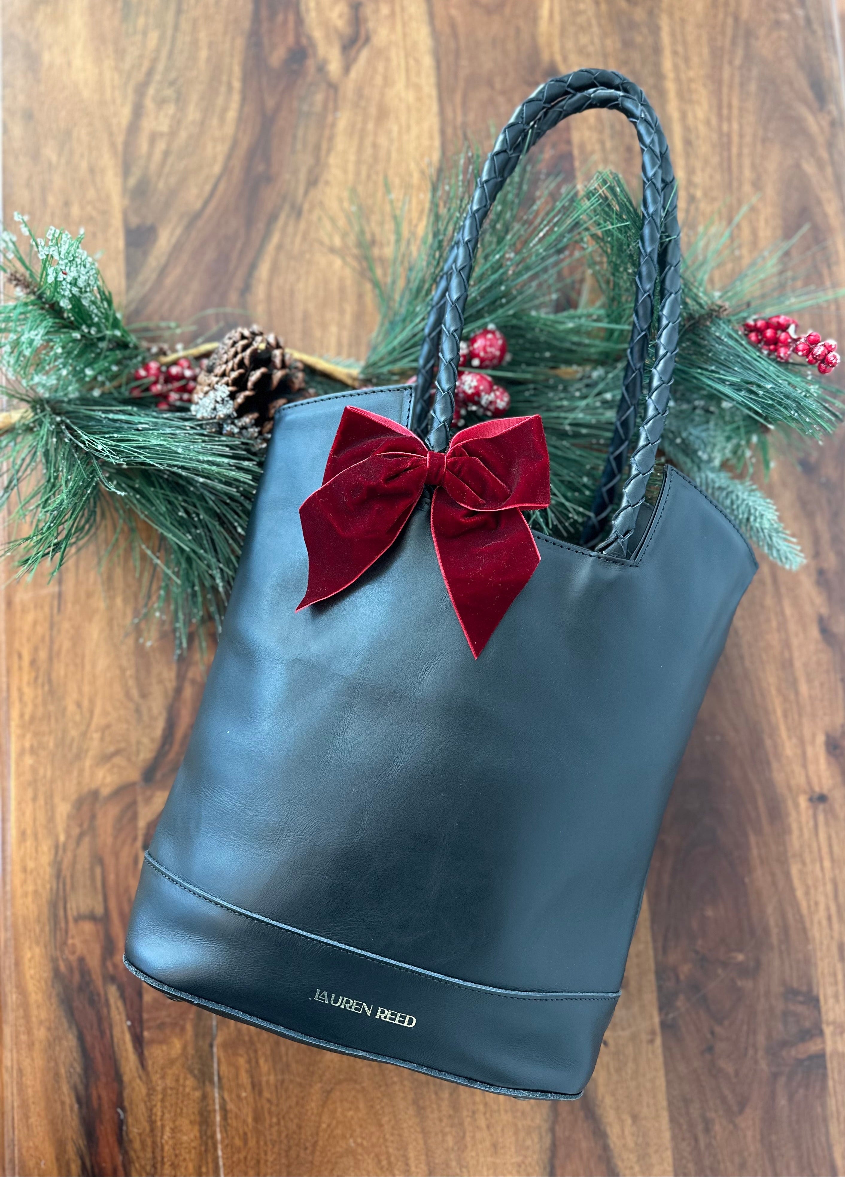 Black handbag with a red bow and Christmas decorations on a wooden surface