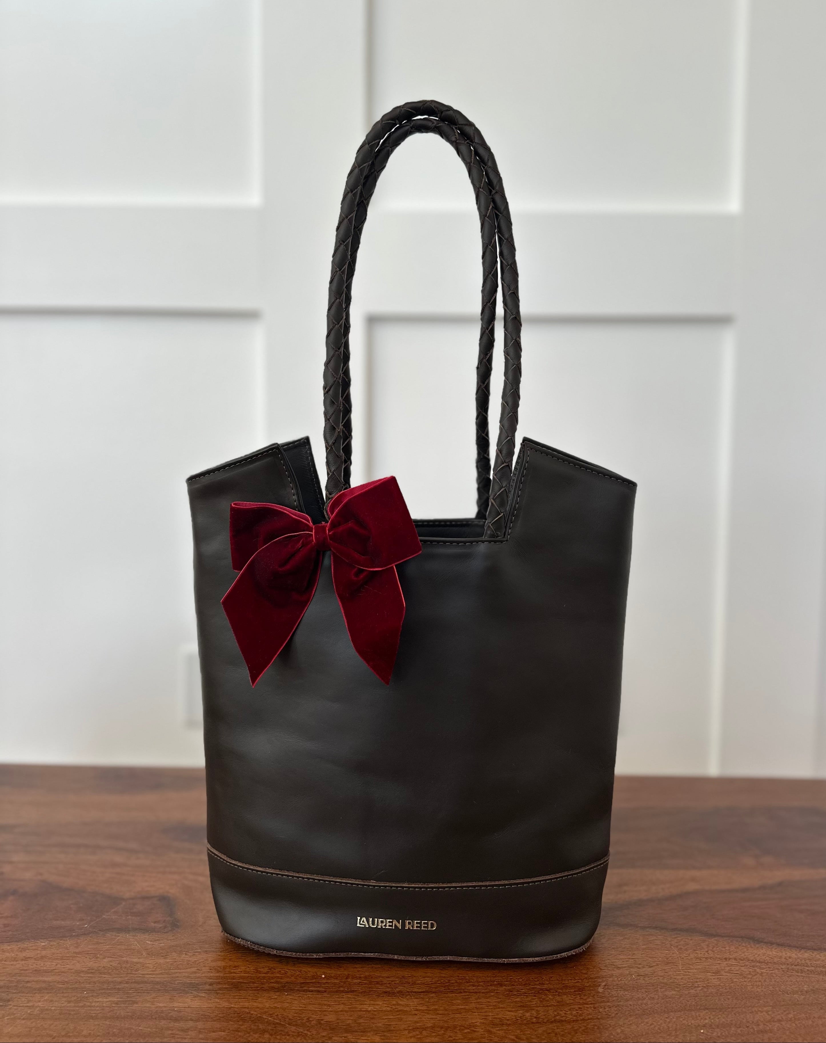 Black tote bag with a red bow on a wooden surface and white paneled wall background