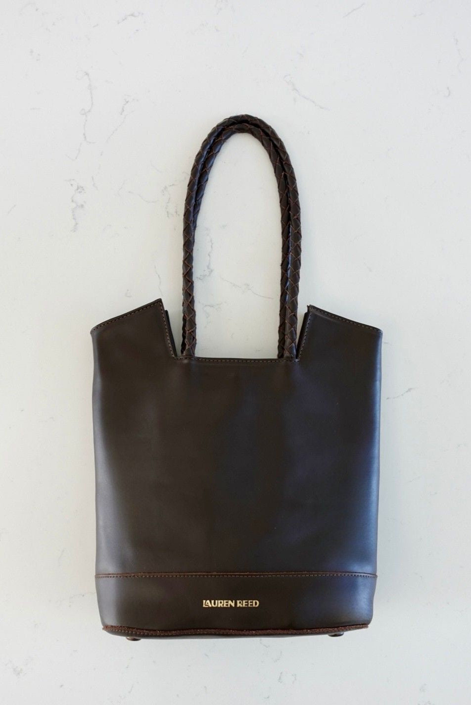 Brown leather tote bag with braided handle on a white background