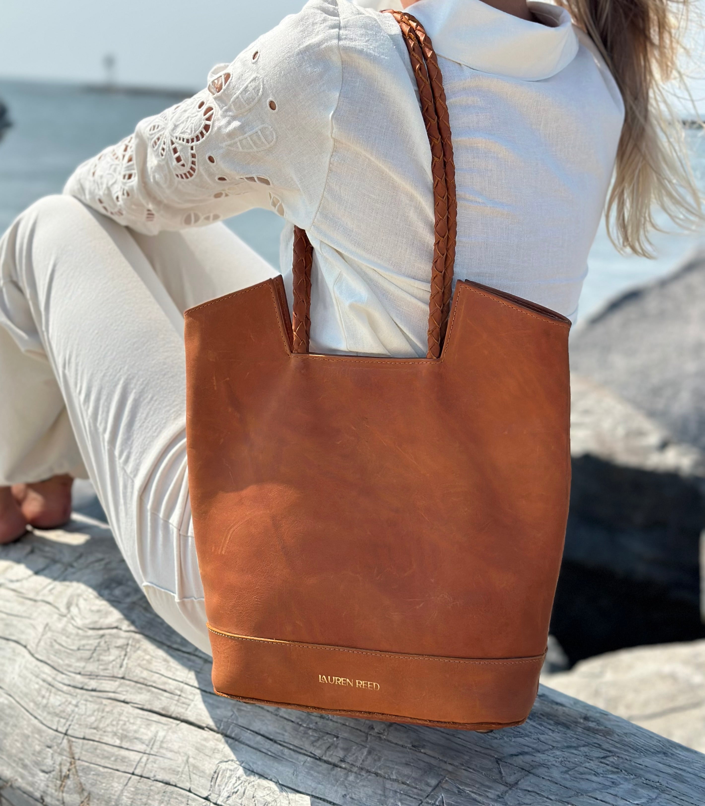 Person sitting by a body of water wearing a tan leather tote bag.
