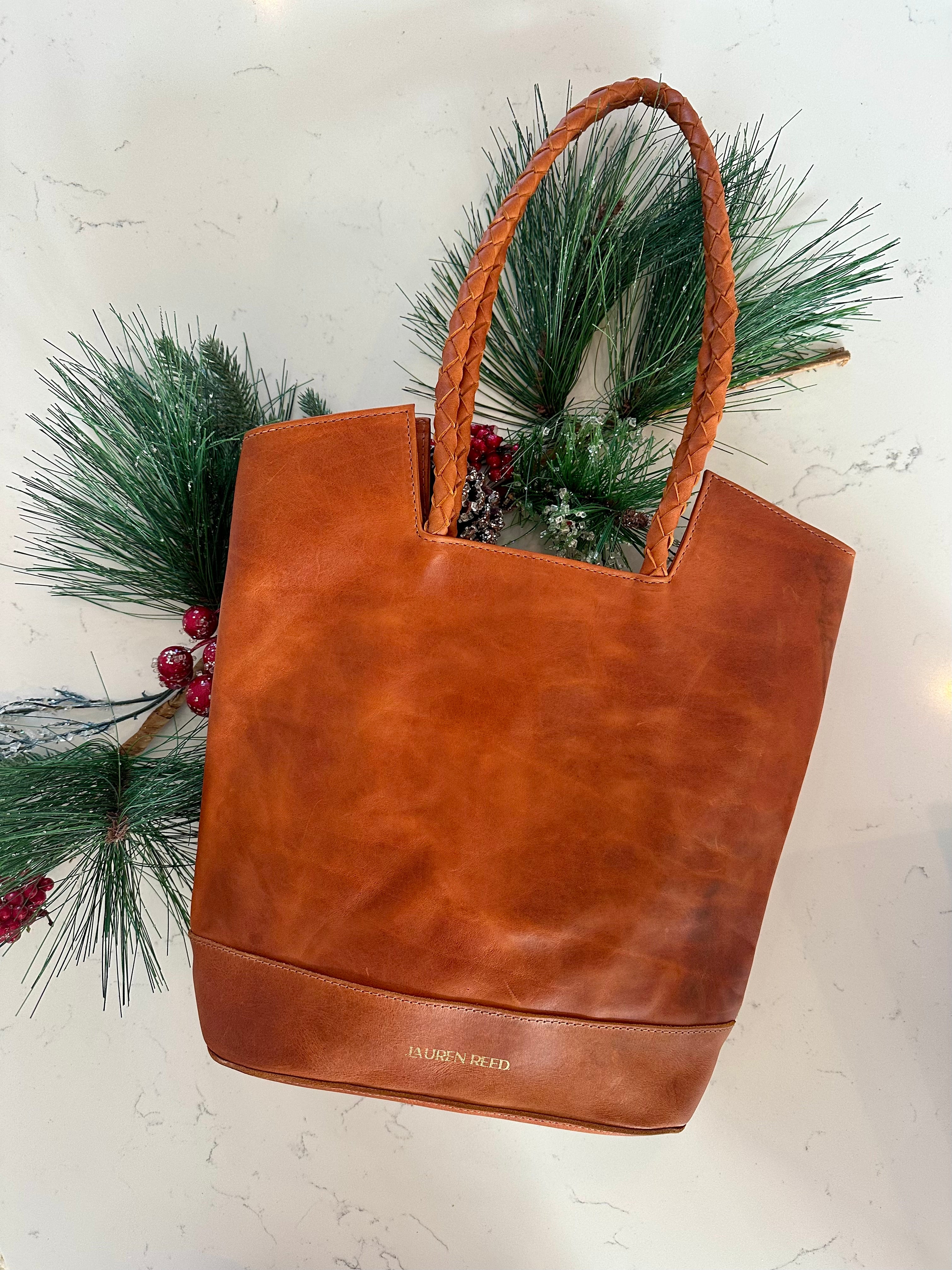 Tan leather tote bag with 'Lauren Reed' branding on a white background with greenery.