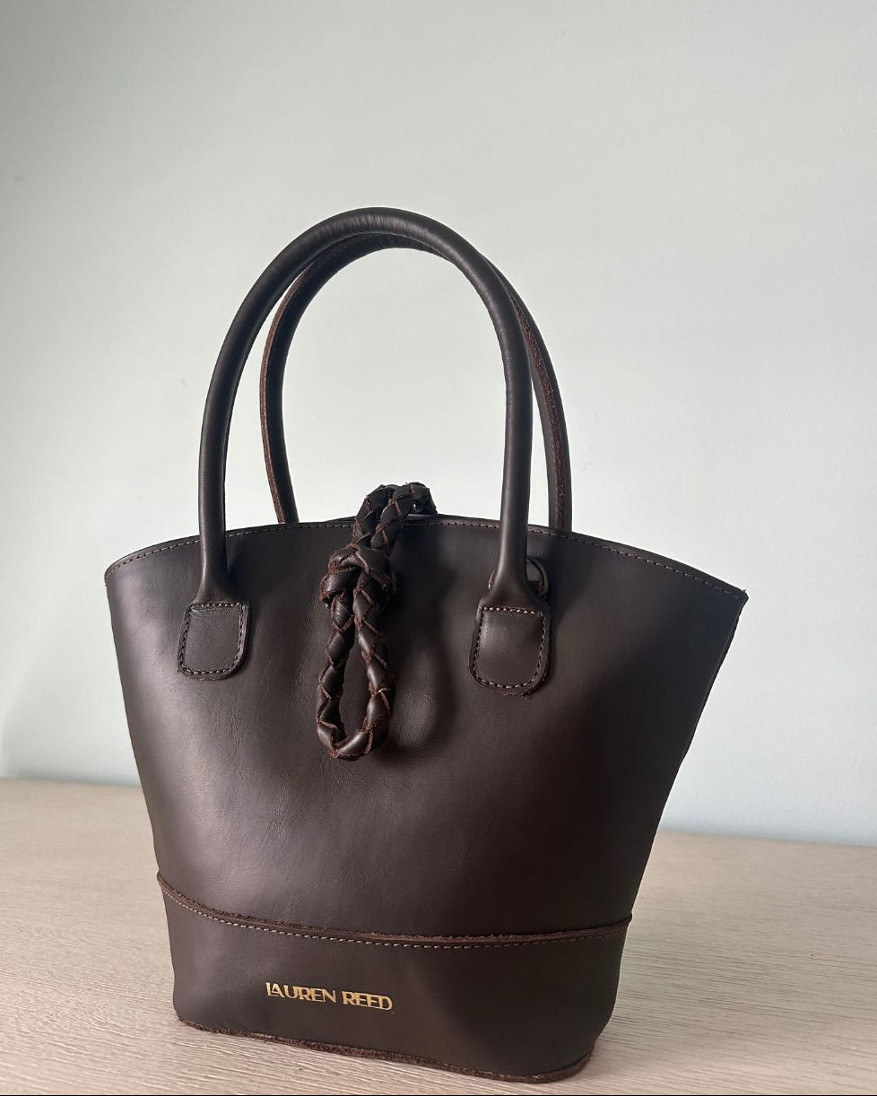 Brown leather handbag with a knot detail on a light surface and light gray background
