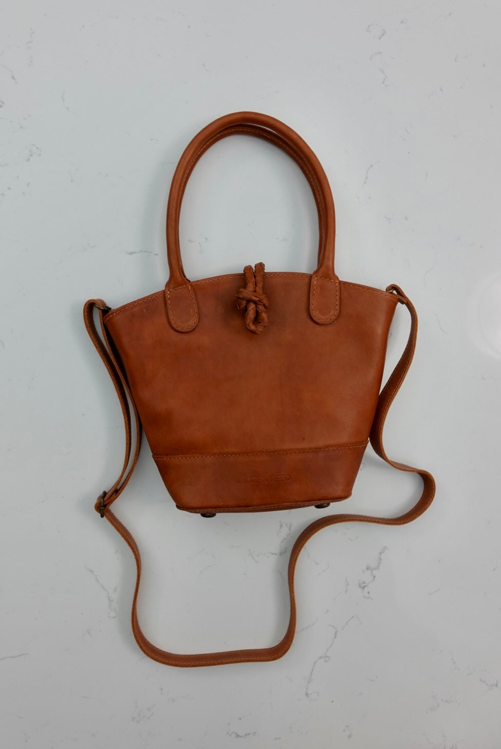 Tan leather handbag with a strap on a light gray background