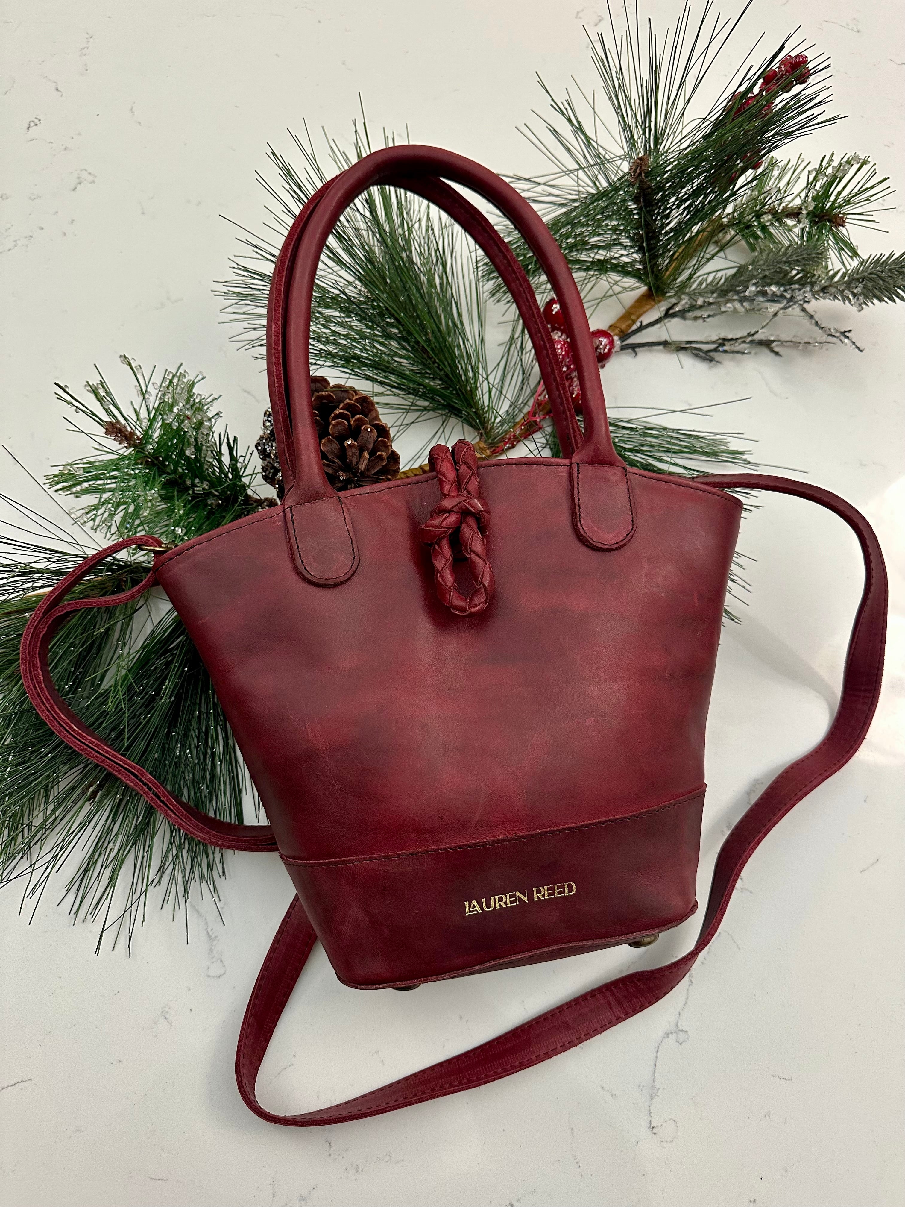 Red handbag with a strap on a white surface with greenery
