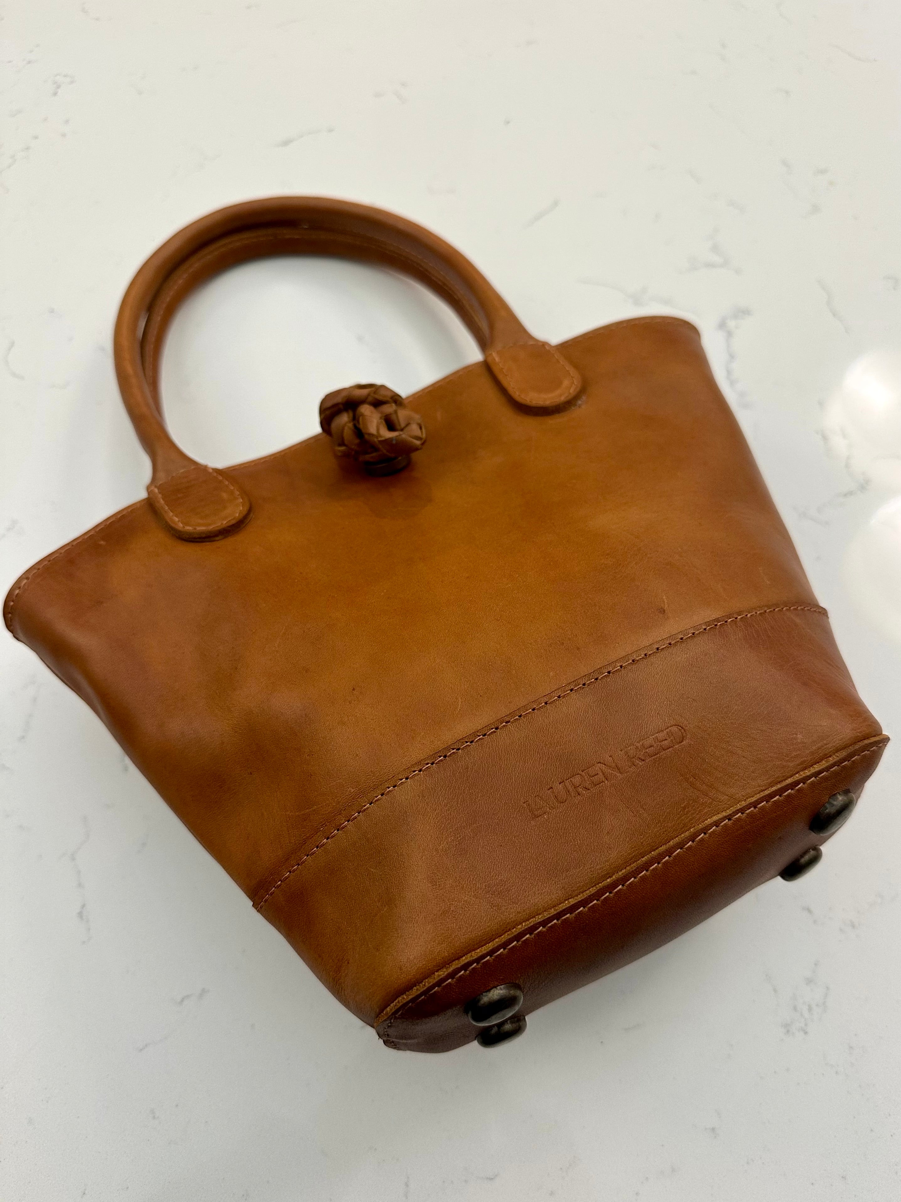 Tan leather handbag with a visible brand logo on a light background