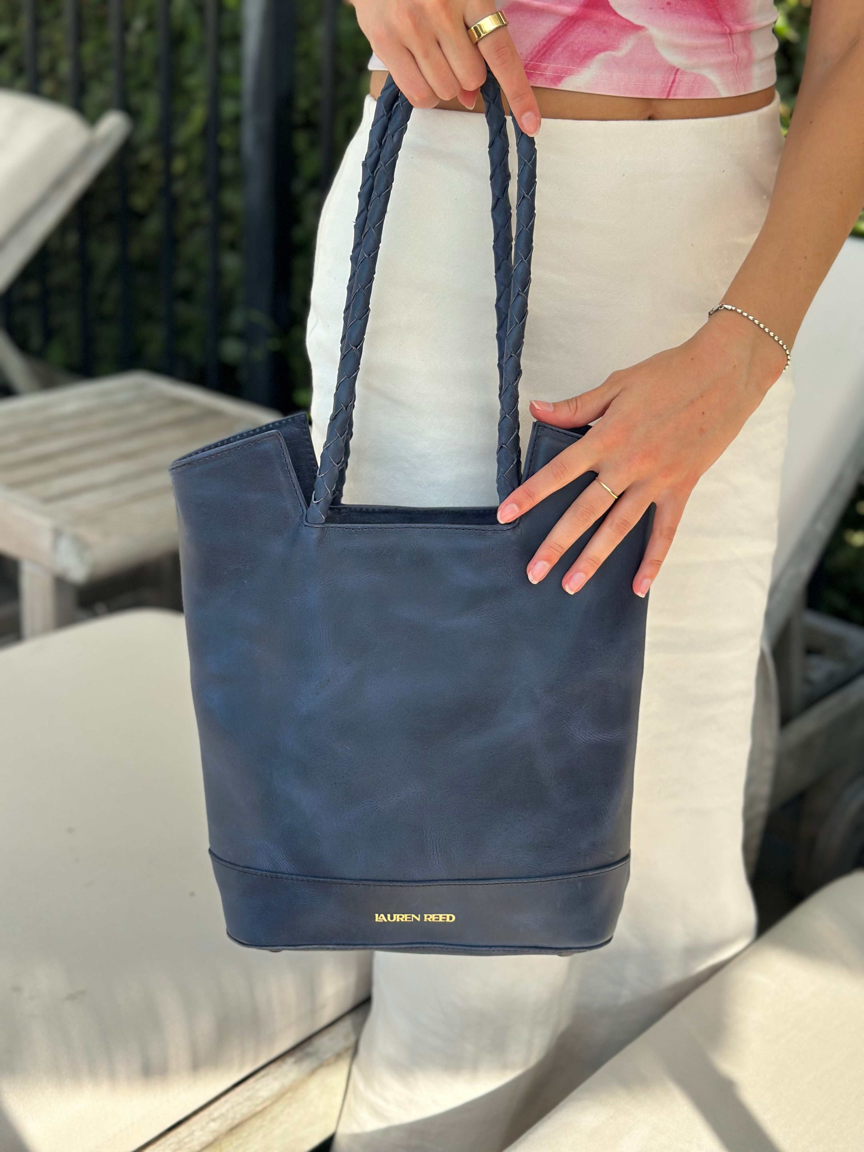 Person holding a blue tote bag with 'Lauren Reed' branding outdoors.