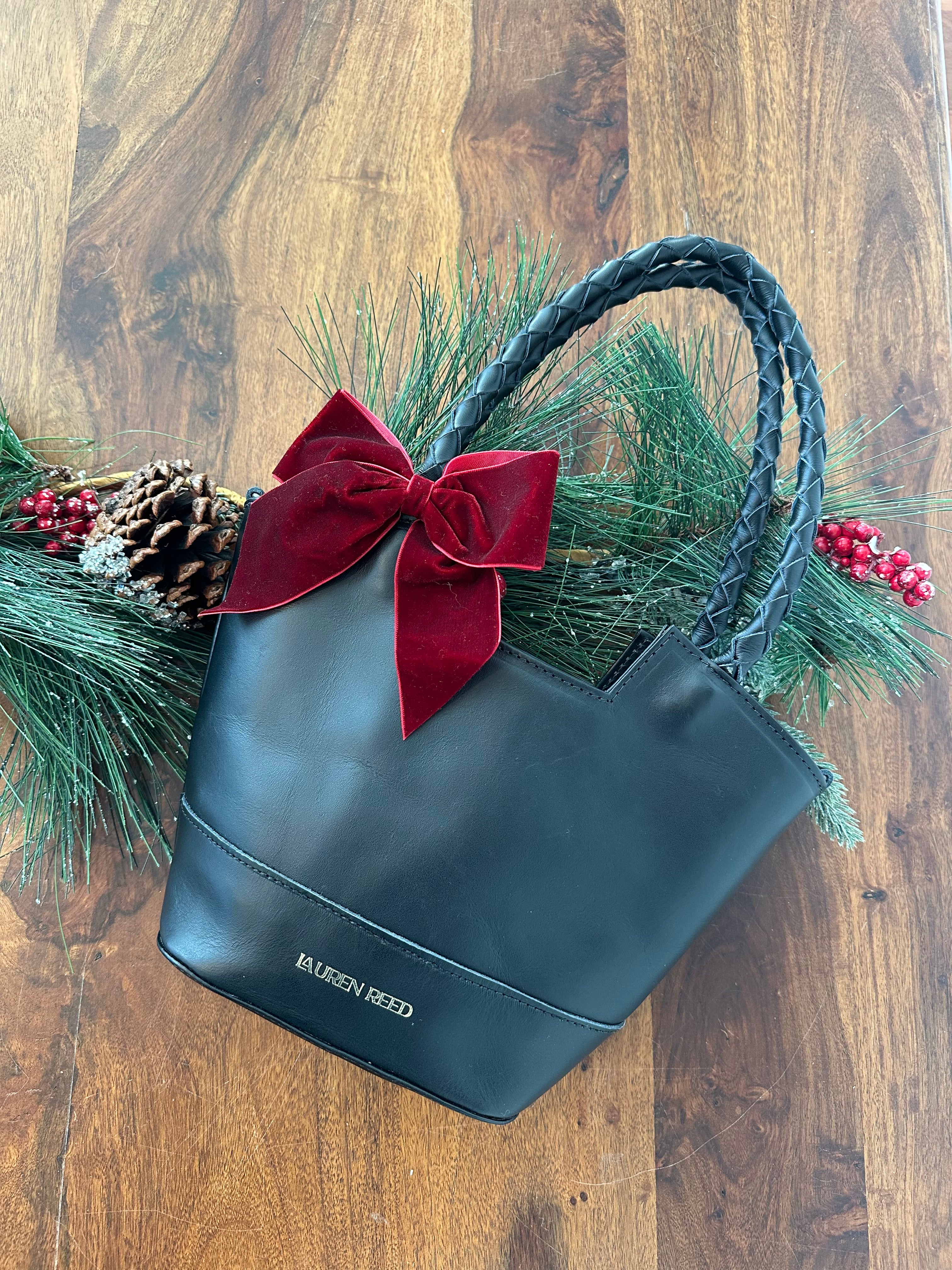 Black handbag with a red bow and Christmas decorations on a wooden surface