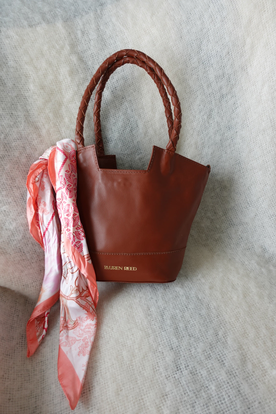 Brown leather handbag with a red and white patterned scarf on a light gray background