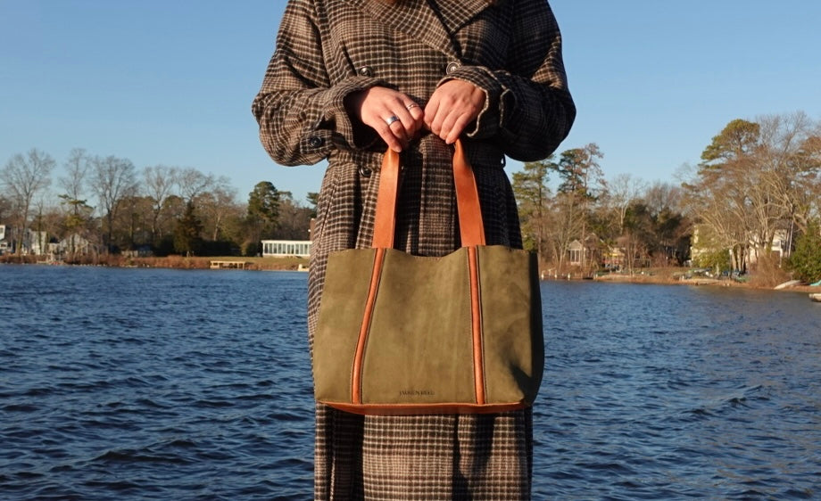 Person holding a green tote bag by a body of water with trees in the background