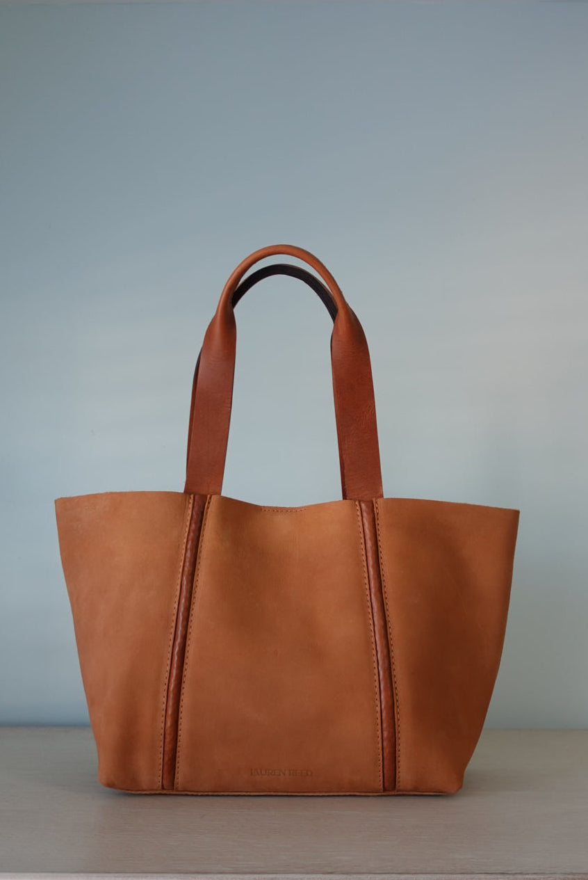 Brown nubuck leather tote bag on a light blue wall