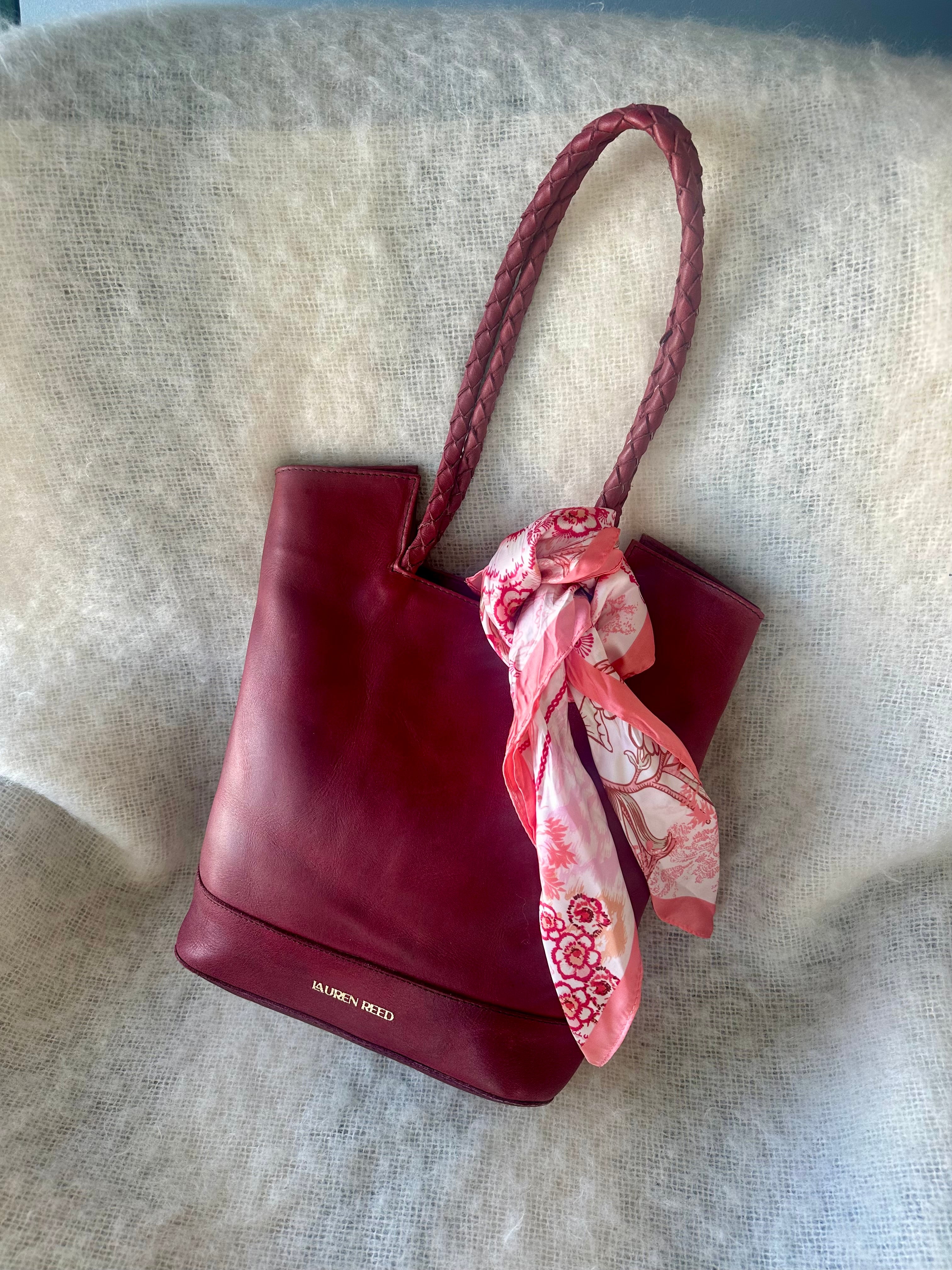 Red handbag with a pink floral scarf draped over it on a textured surface