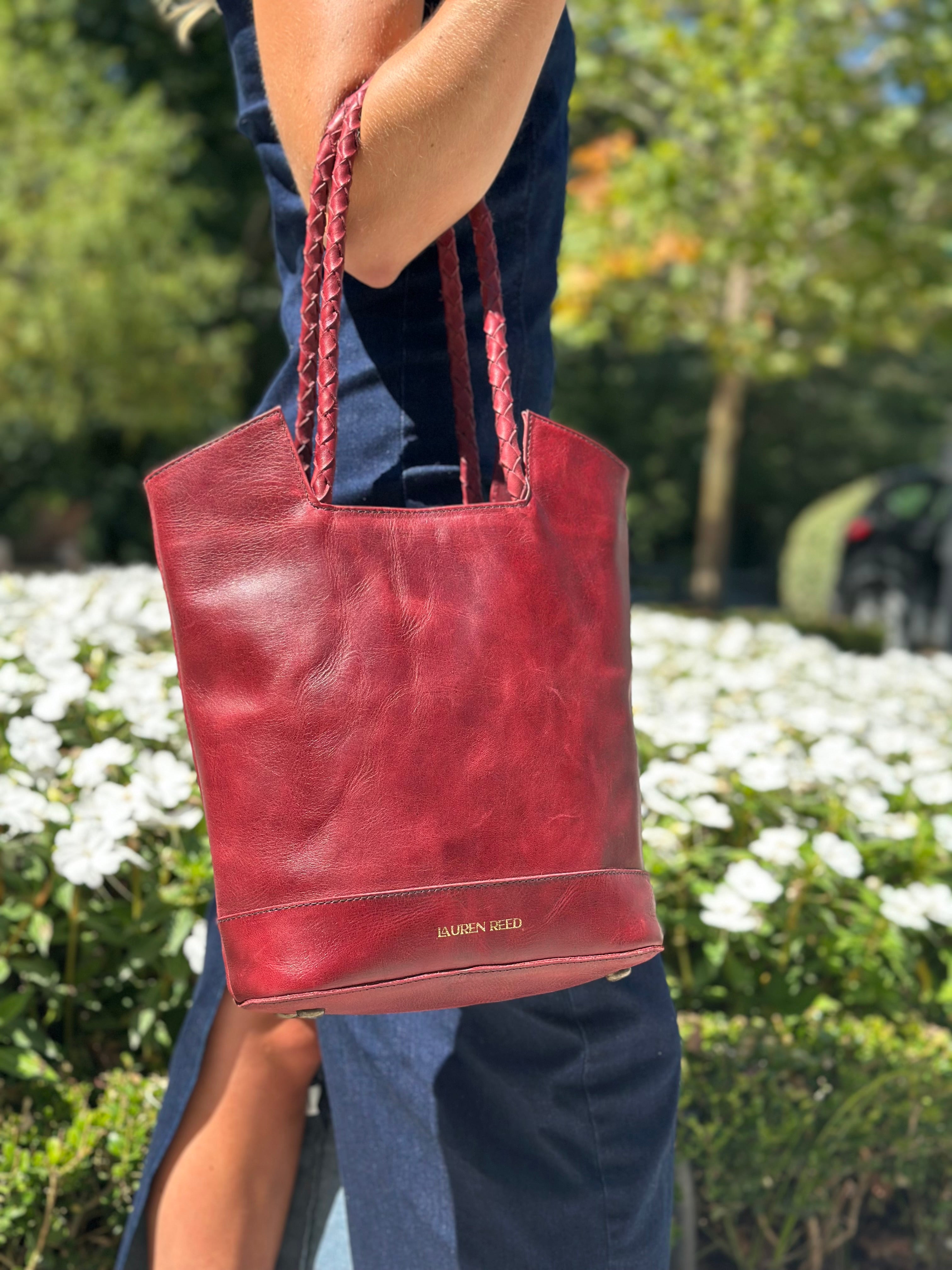 Red leather summer handbag held by a person outdoors with greenery and flower farm