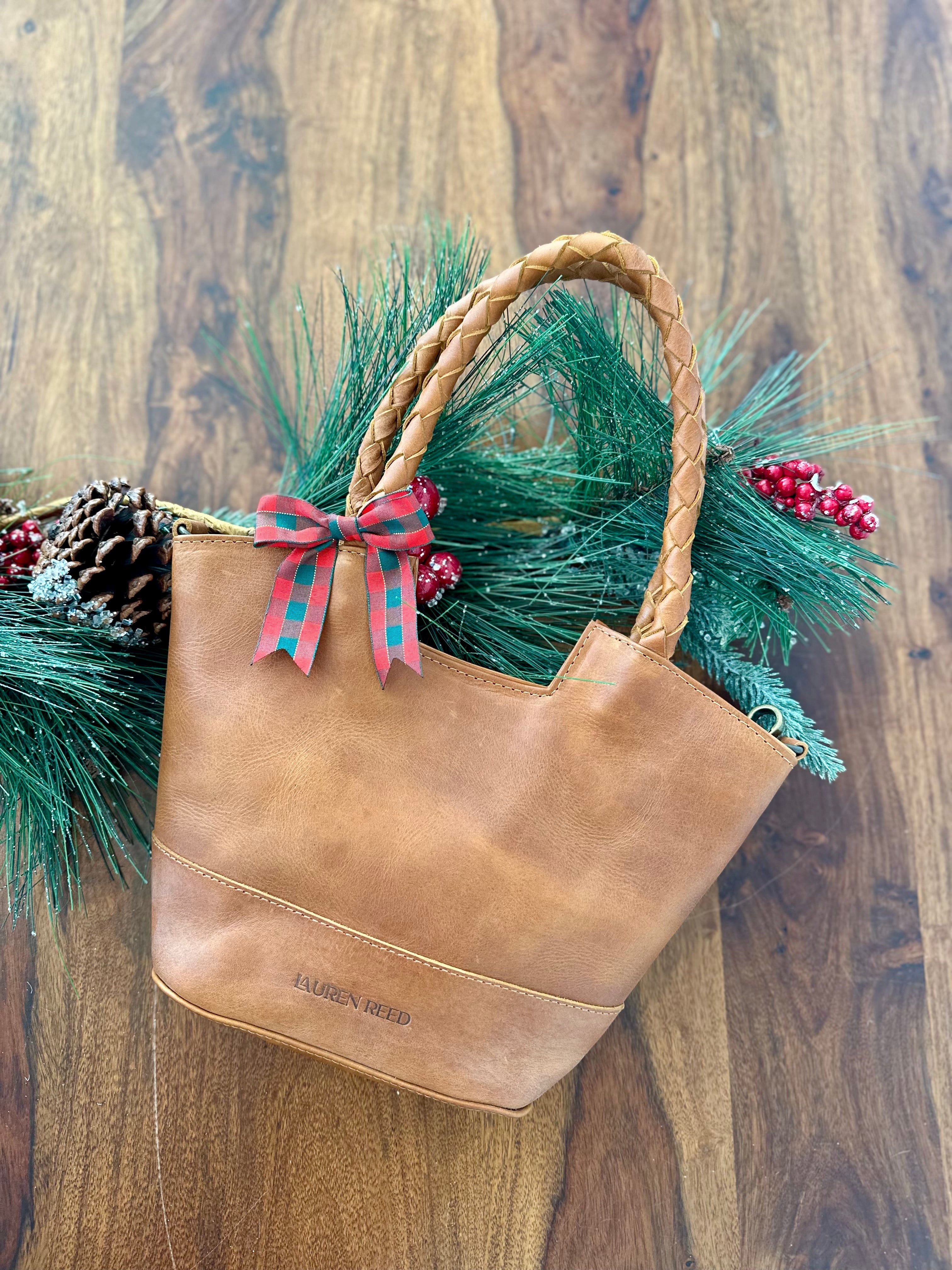 Brown leather bag with a plaid bow and greenery on a wooden background