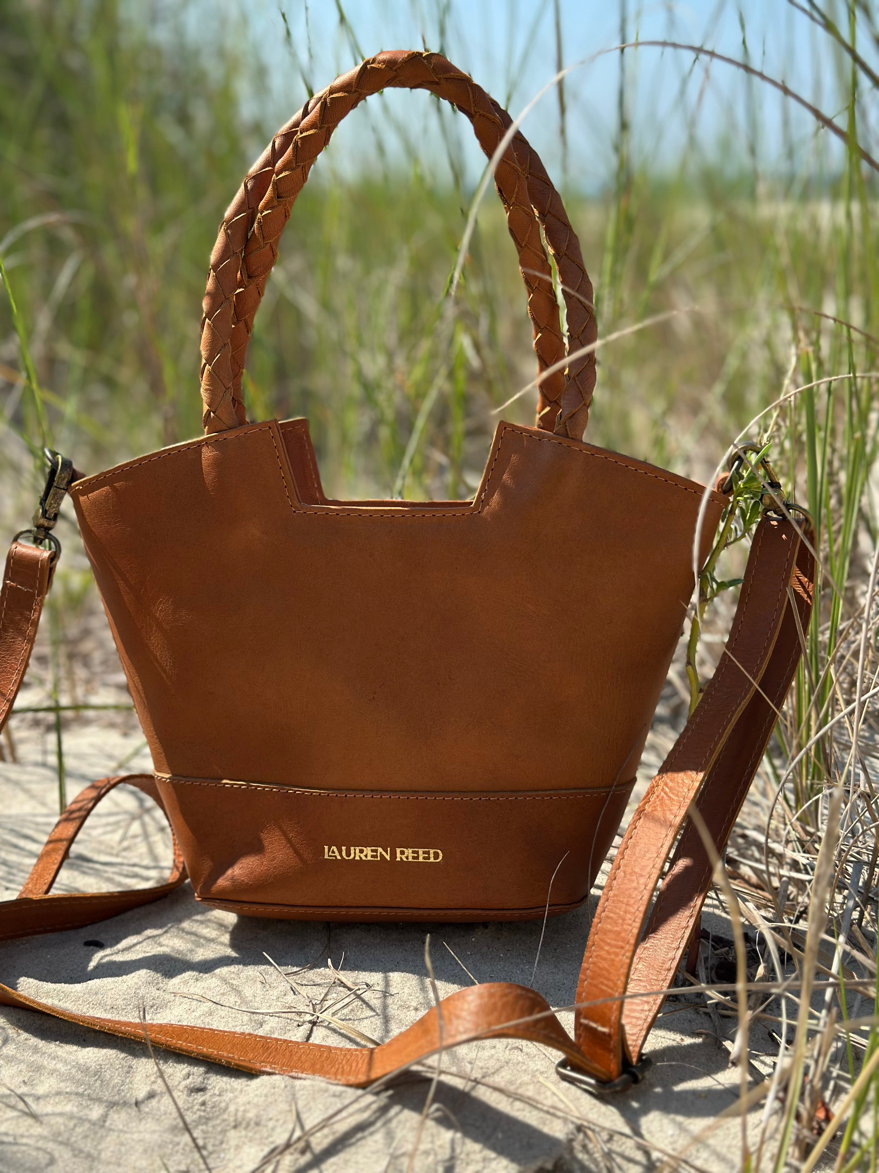 Brown handbag with braided handles and strap on a sandy background