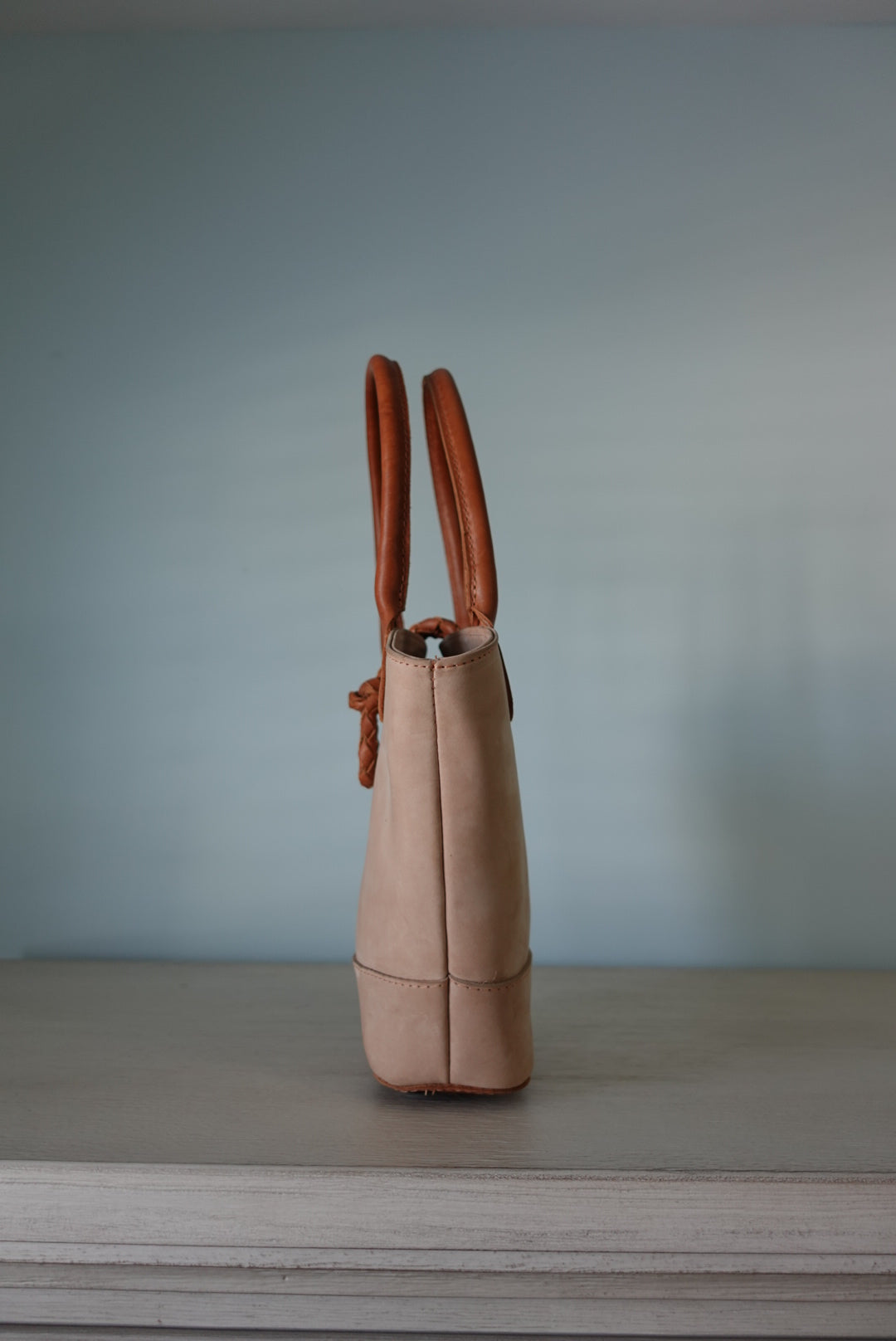 Cream Beige leather summer handbag with brown handles on a light blue background